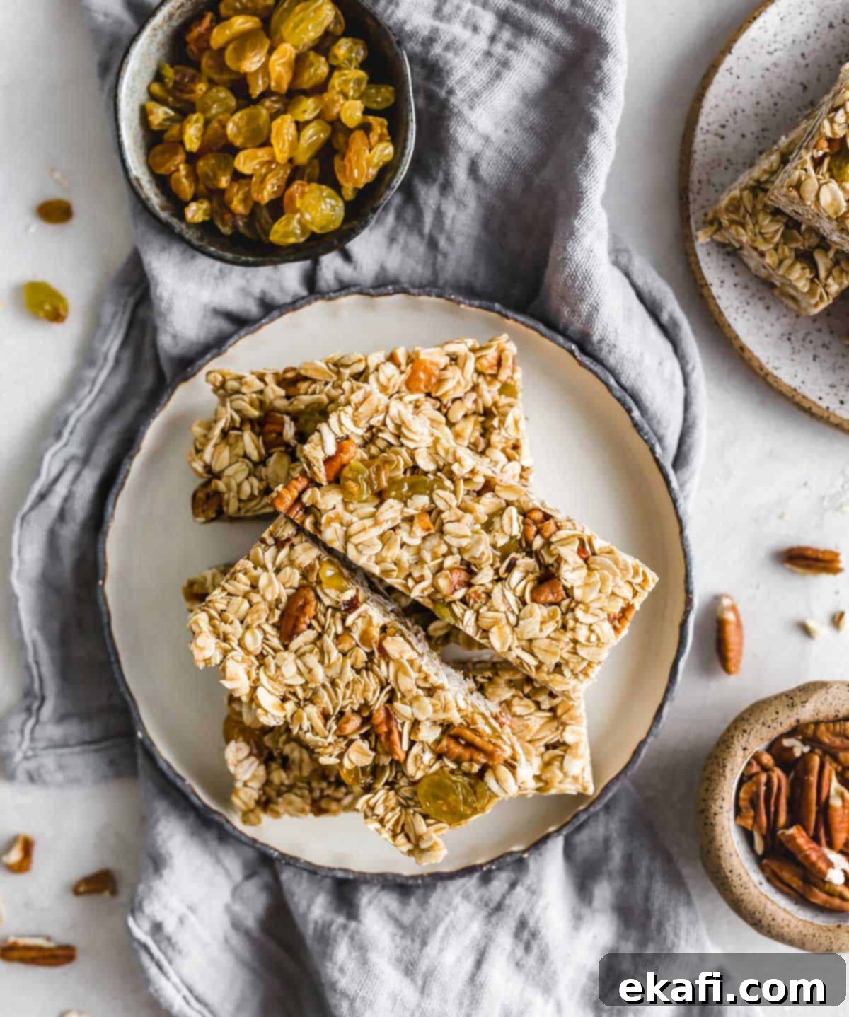 Μπάρες Γκρανόλα Βρώμης Σταφίδας 9 Homemade Oatmeal Raisin Granola Bars with nuts and golden raisins on a black rimmed white plate on a light gray linen napkin.