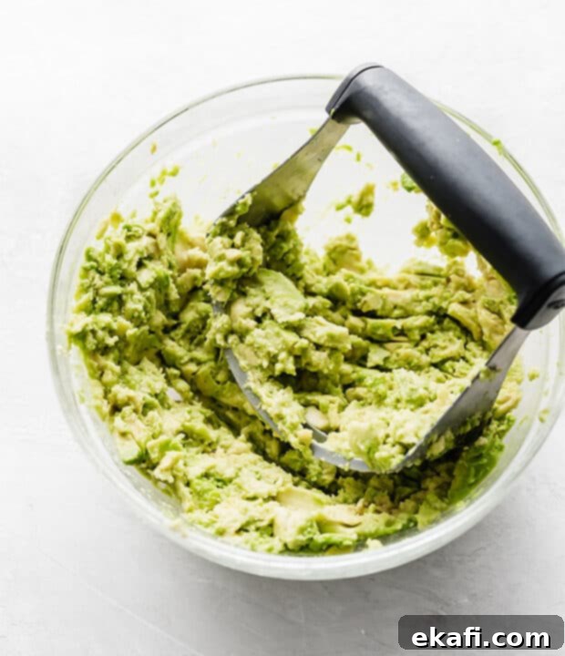 Creamy Avocado Chicken Wraps 5 A glass bowl with a pastry cutter mashing avocados, demonstrating a quick preparation step.