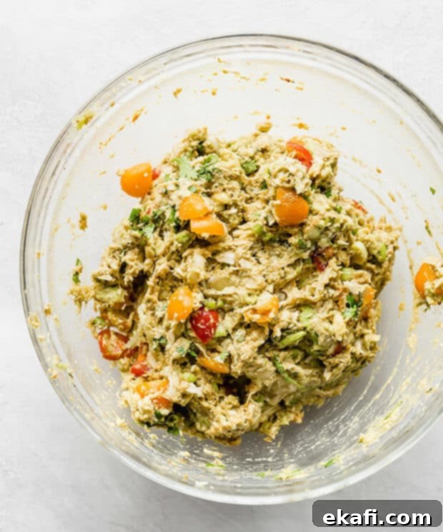 Creamy Avocado Chicken Wraps 6 A bowl with vibrant Avocado Chicken Wraps ingredients: shredded chicken, mashed avocado, chopped tomatoes, and various spices.