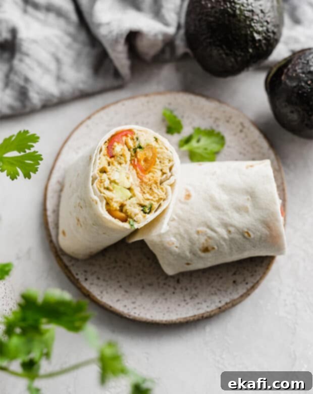 Creamy Avocado Chicken Wraps 8 An Avocado Chicken Wrap cut in half, revealing the fresh, colorful filling, served on a plate.