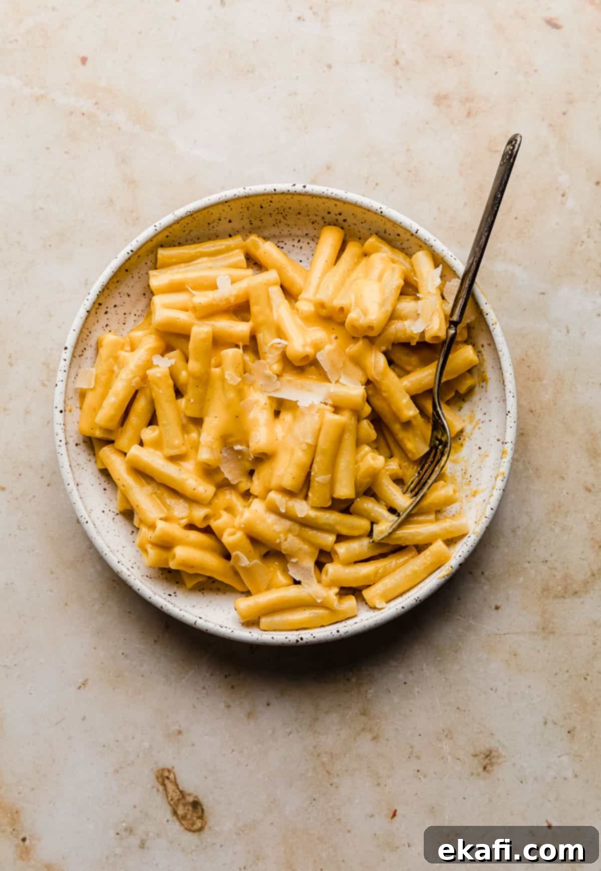 Velvety Butternut Squash Pasta 2 A white plate with creamy roasted Butternut Squash Pasta on it, against a tan marble background. The pasta is a rich orange color, garnished with fresh herbs and a sprinkle of Parmesan cheese, highlighting its inviting texture.