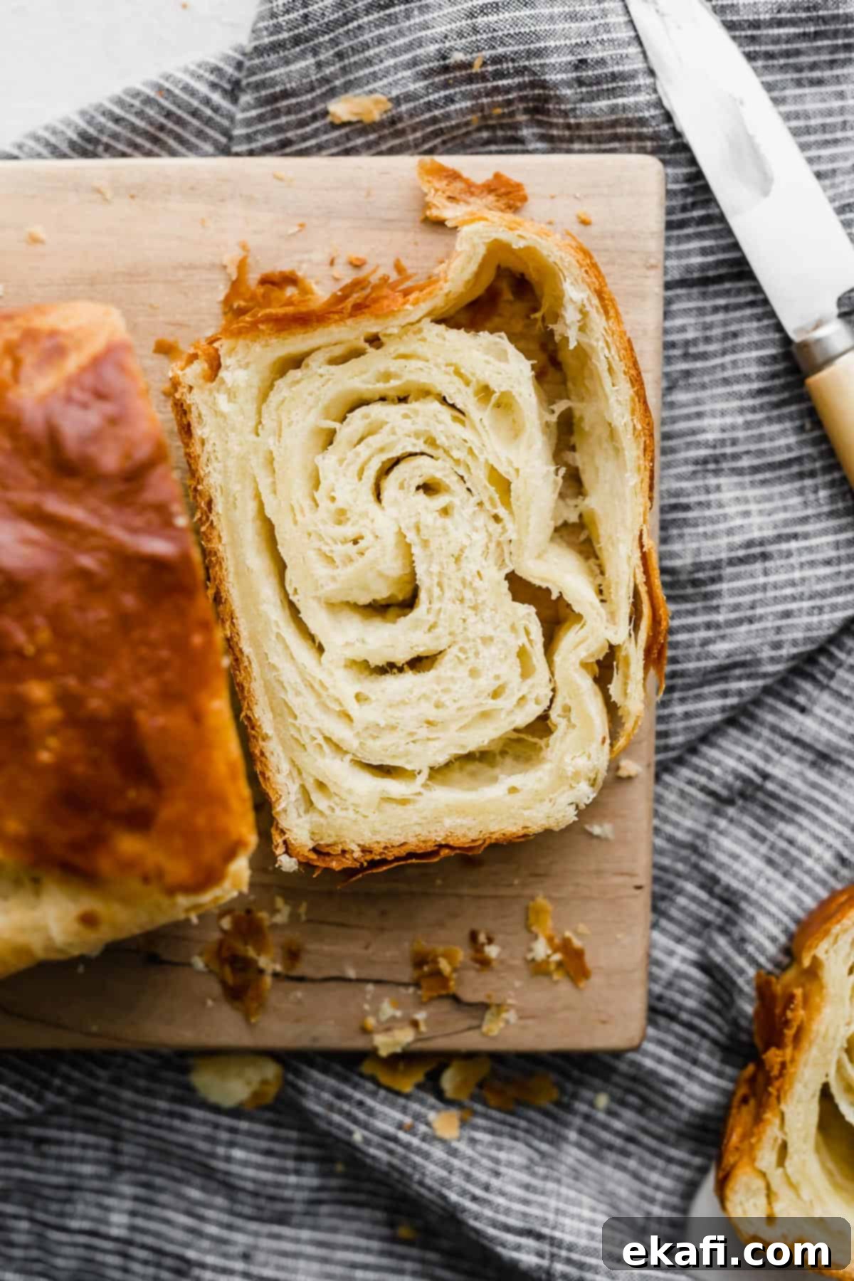 Pillowy Flaky Brioche 2 A perfectly sliced, golden brown flaky brioche bread on a wooden cutting board, showcasing its numerous airy layers.