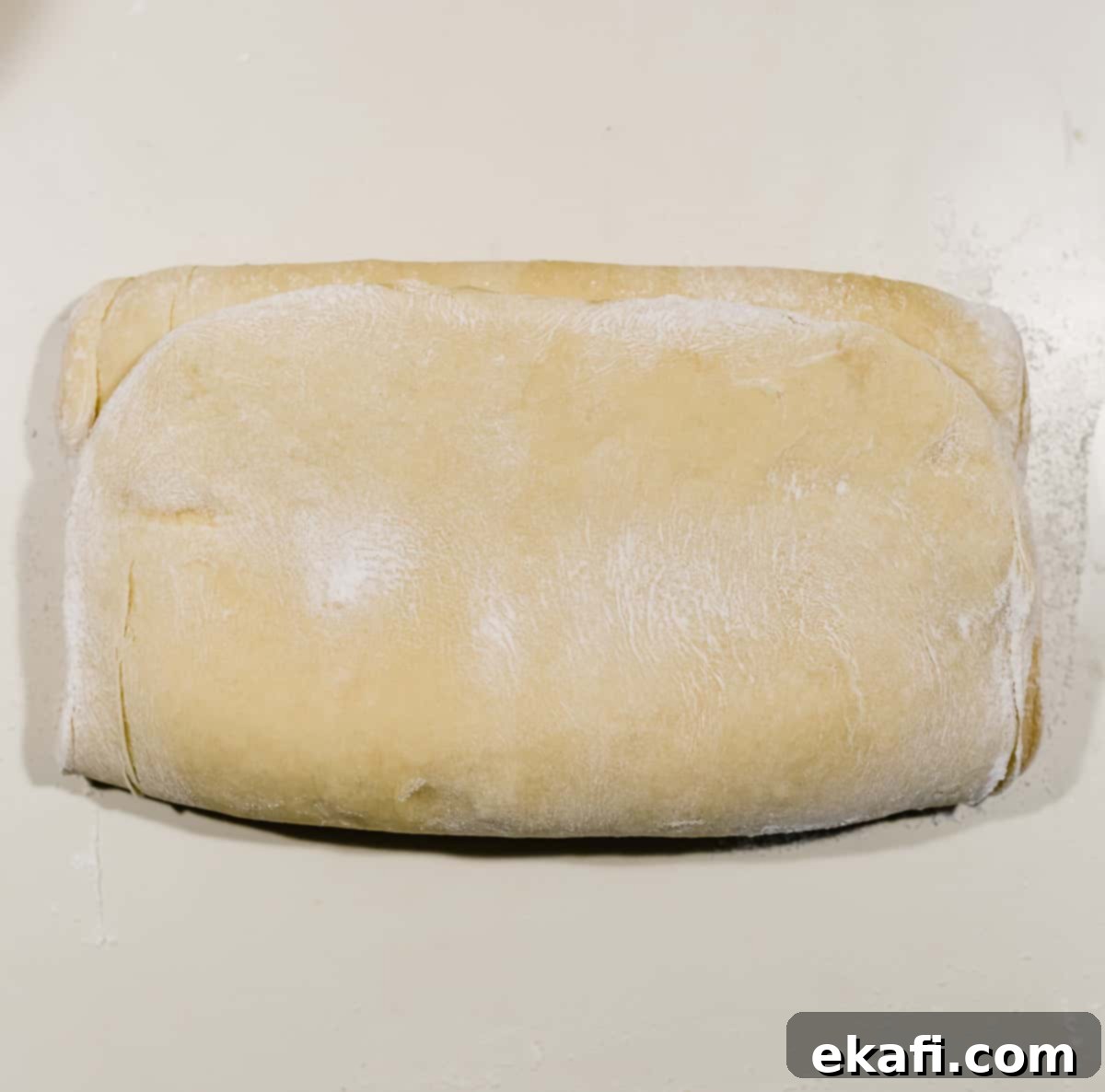 Pillowy Flaky Brioche 11 A perfectly folded rectangle of flaky brioche bread dough on a white countertop, completing one turn of lamination.