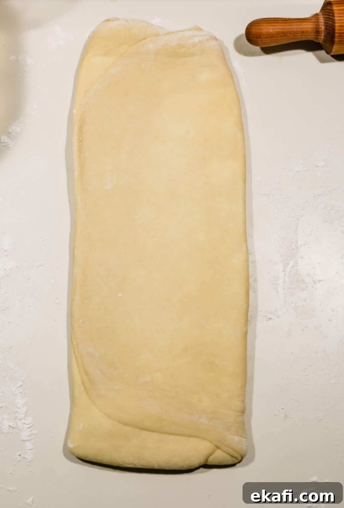 Pillowy Flaky Brioche 12 Brioche bread dough rolled out to a long rectangular shape on a white countertop, prepared for the next fold.