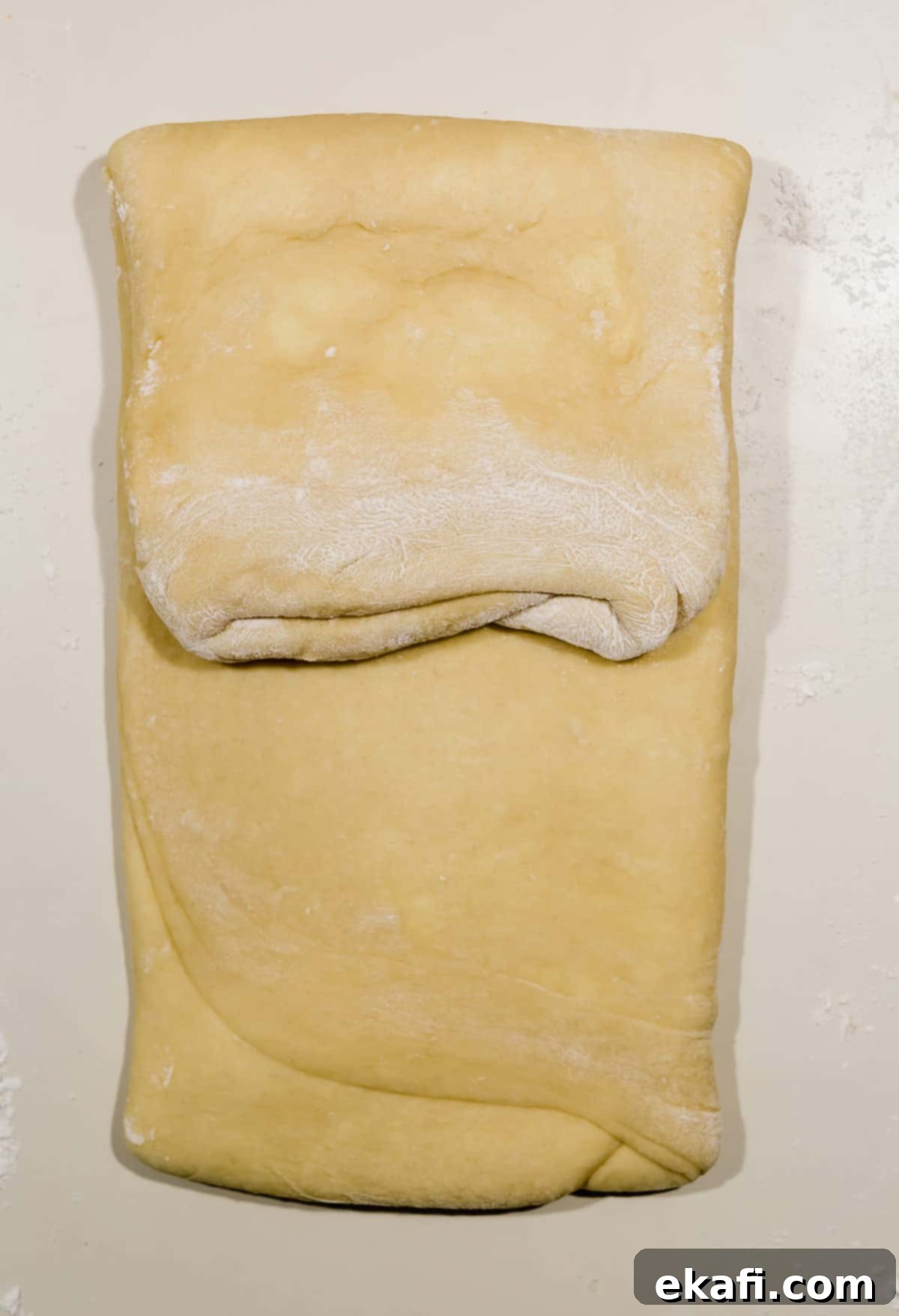 Pillowy Flaky Brioche 13 The process of laminating brioche bread, showing the top half of the dough folded over itself for a new layer.