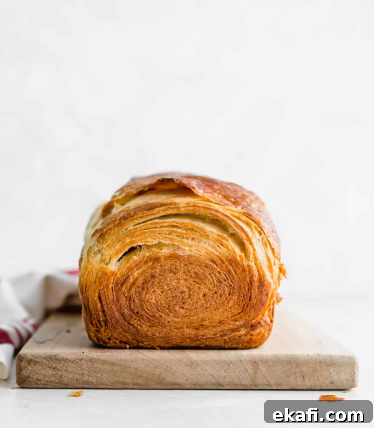 Pillowy Flaky Brioche 16 A beautifully golden and flaky brioche loaf resting on a rustic wooden cutting board, set against a clean white background.
