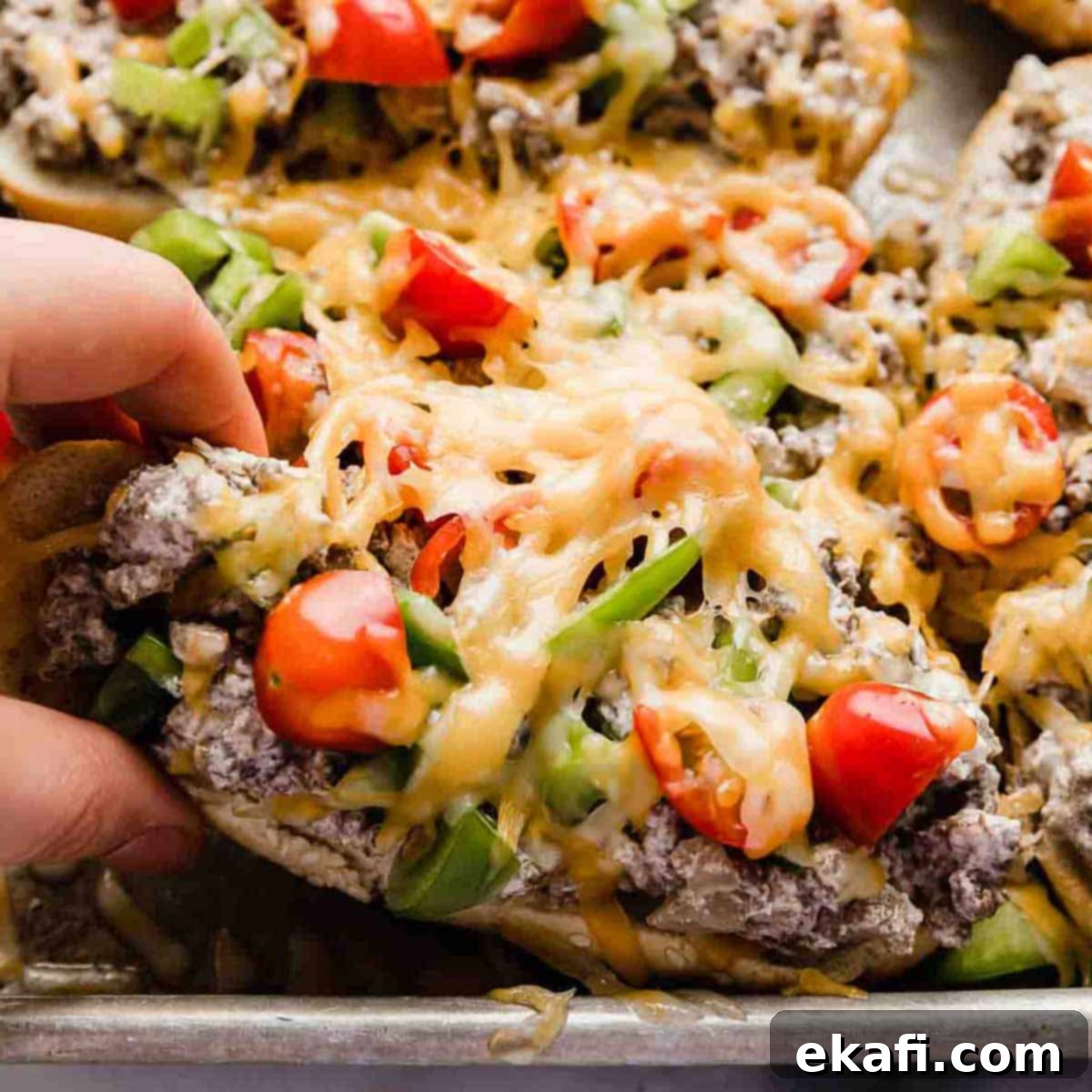 Happy Tummies Happy Kids 13 A hand reaching for a delicious Beef Stroganoff Sandwich, generously topped with fresh tomatoes, colorful peppers, and melted shredded cheese, highlighting its hearty appeal.