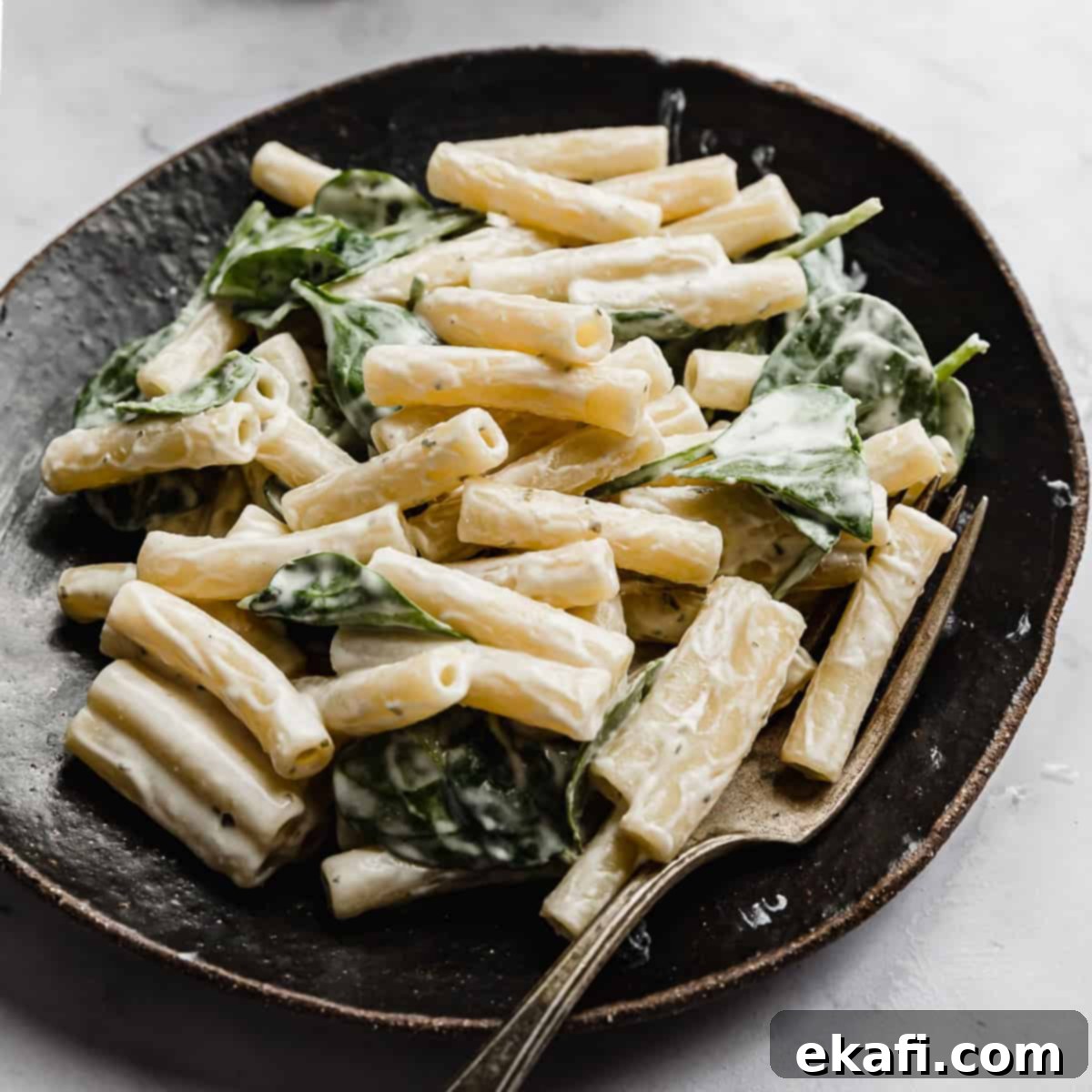 Happy Tummies Happy Kids 18 A chic black plate holds a generous serving of creamy Boursin Pasta, beautifully tossed with vibrant fresh spinach, promising a delightful and quick meal.