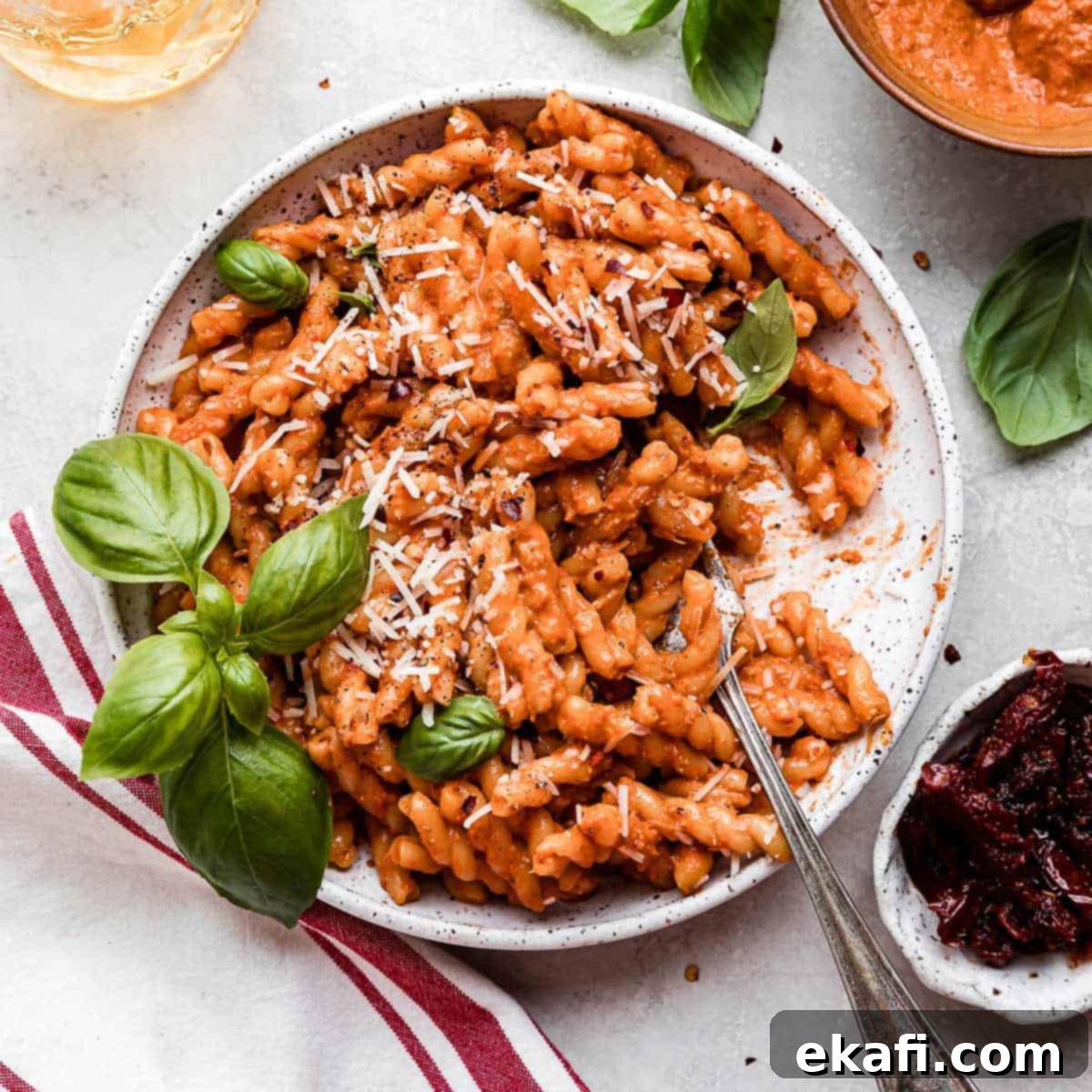 Happy Tummies Happy Kids 3 A white plate filled with Red Pesto Pasta, generously topped with freshly grated parmesan cheese and vibrant green basil leaves, ready to be enjoyed.