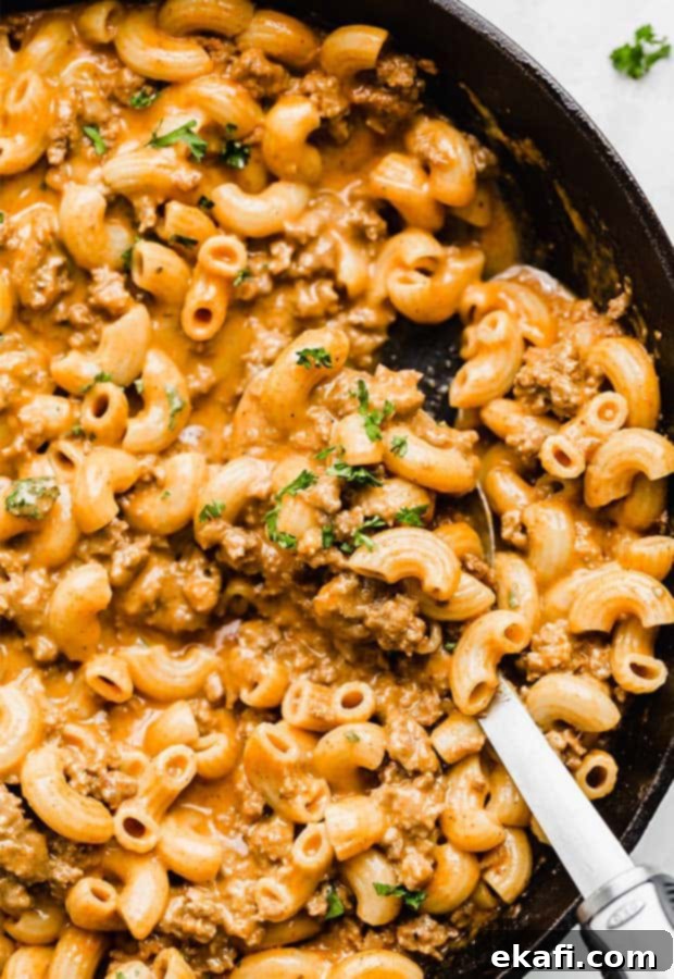 Happy Tummies Happy Kids 21 A close-up photo showcasing a cast iron skillet brimming with macaroni noodles, ground beef, and a rich, cheesy sauce, making for a hearty homemade hamburger helper.