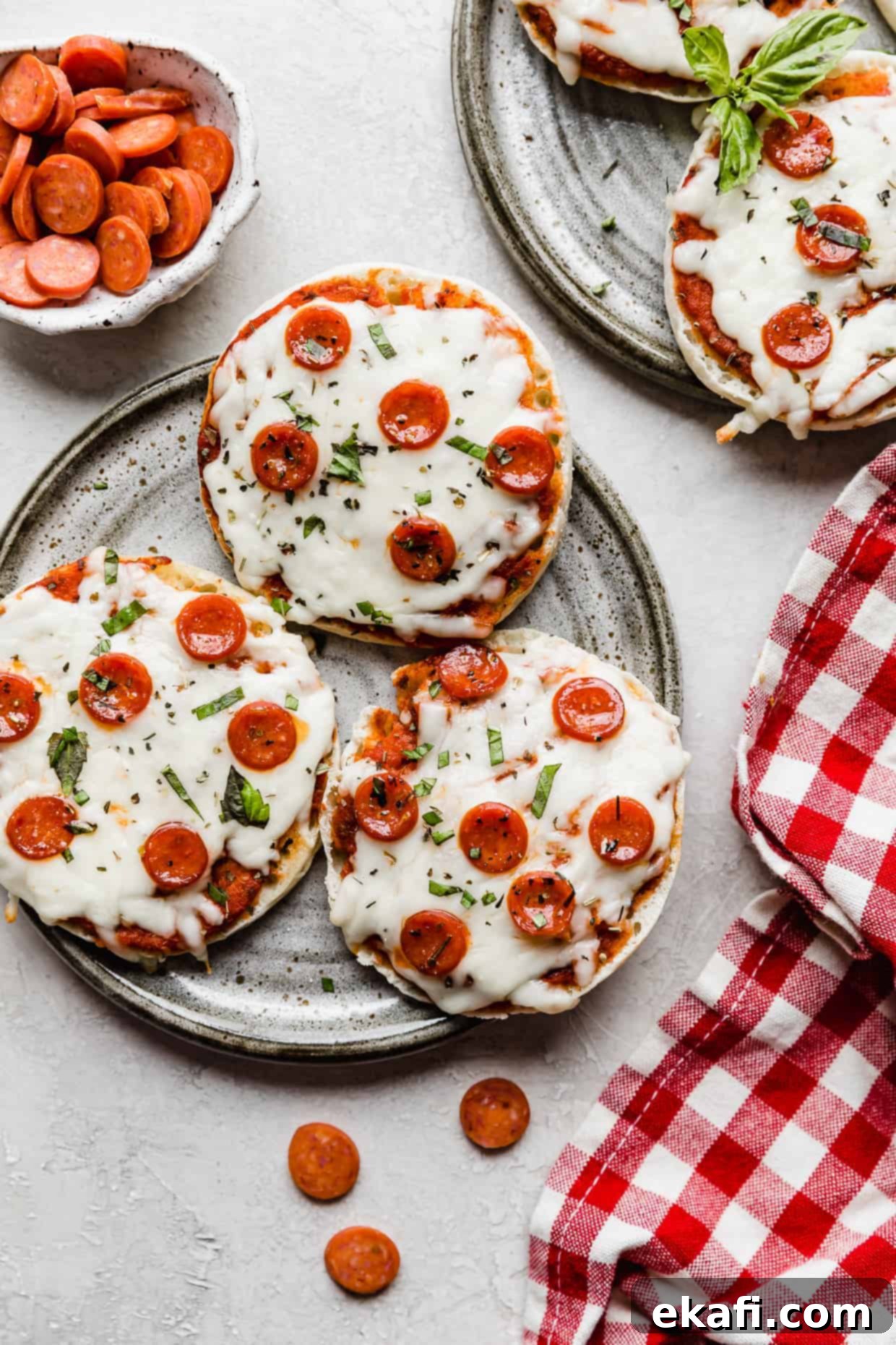 Happy Tummies Happy Kids 22 Three perfectly cooked English muffin pizzas, generously topped with mini pepperonis, artfully arranged on a chic gray plate, making for a quick and satisfying meal.