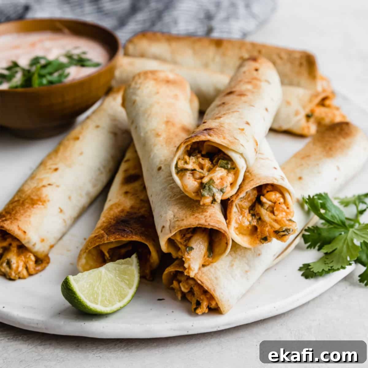 Happy Tummies Happy Kids 4 Perfectly stacked golden-brown Baked Chicken Taquitos on a pristine white plate, garnished with fresh parsley in the background, ready to be dipped.