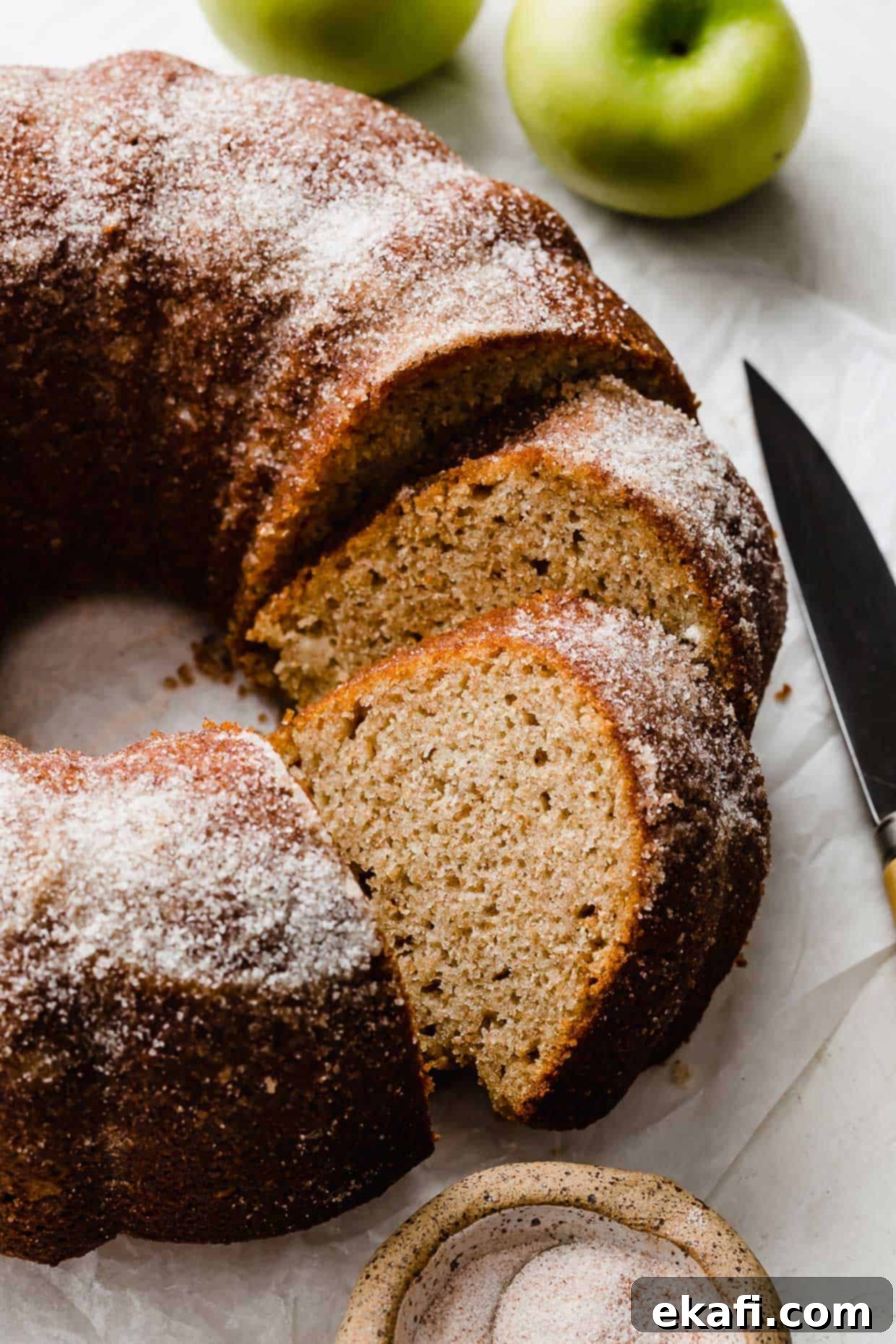 Πώς να αξιοποιήσετε τα μήλα 11 Ένα κέικ Bundt με μηλίτη, πασπαλισμένο με ζάχαρη, με πράσινα μήλα στο φόντο.