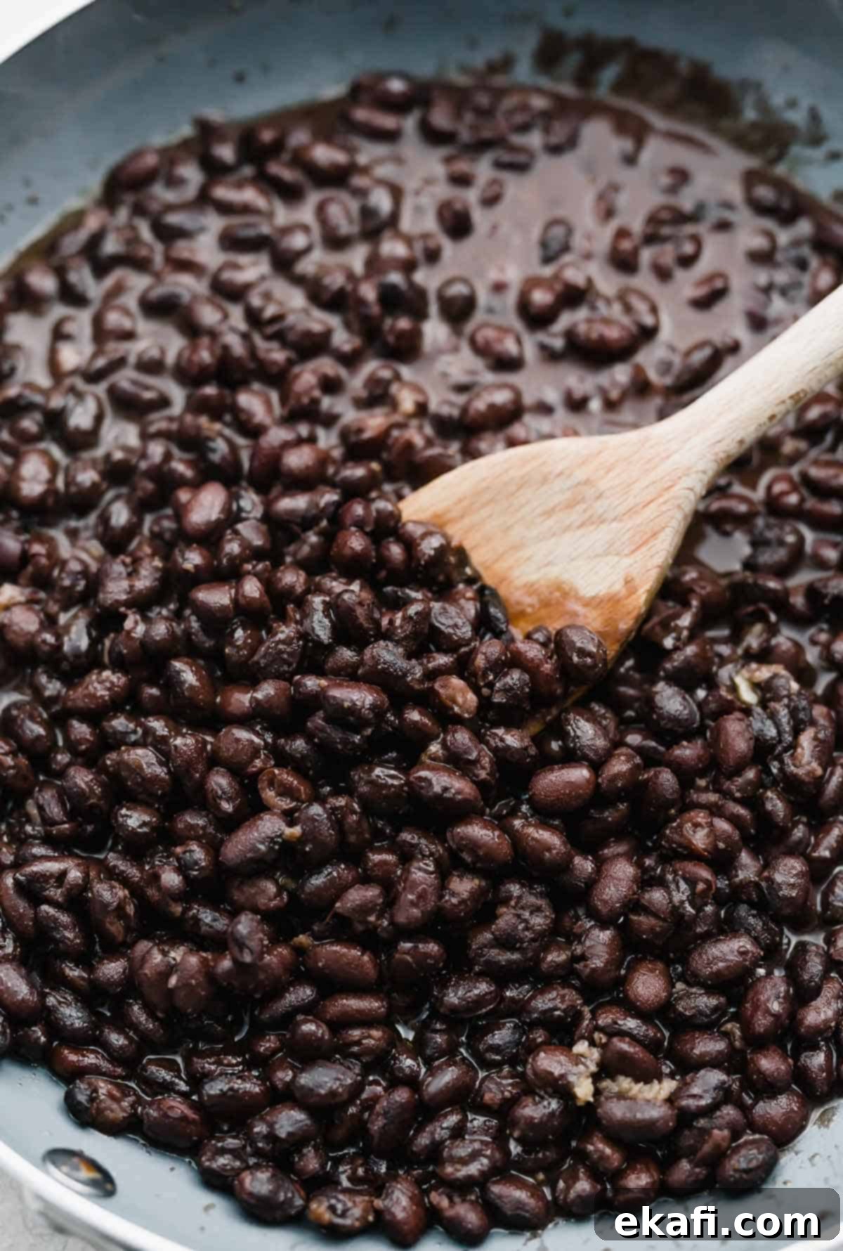 Cafe Rio Style Black Beans 4 Canned black beans being cooked in a gray skillet, stirring with a spoon.