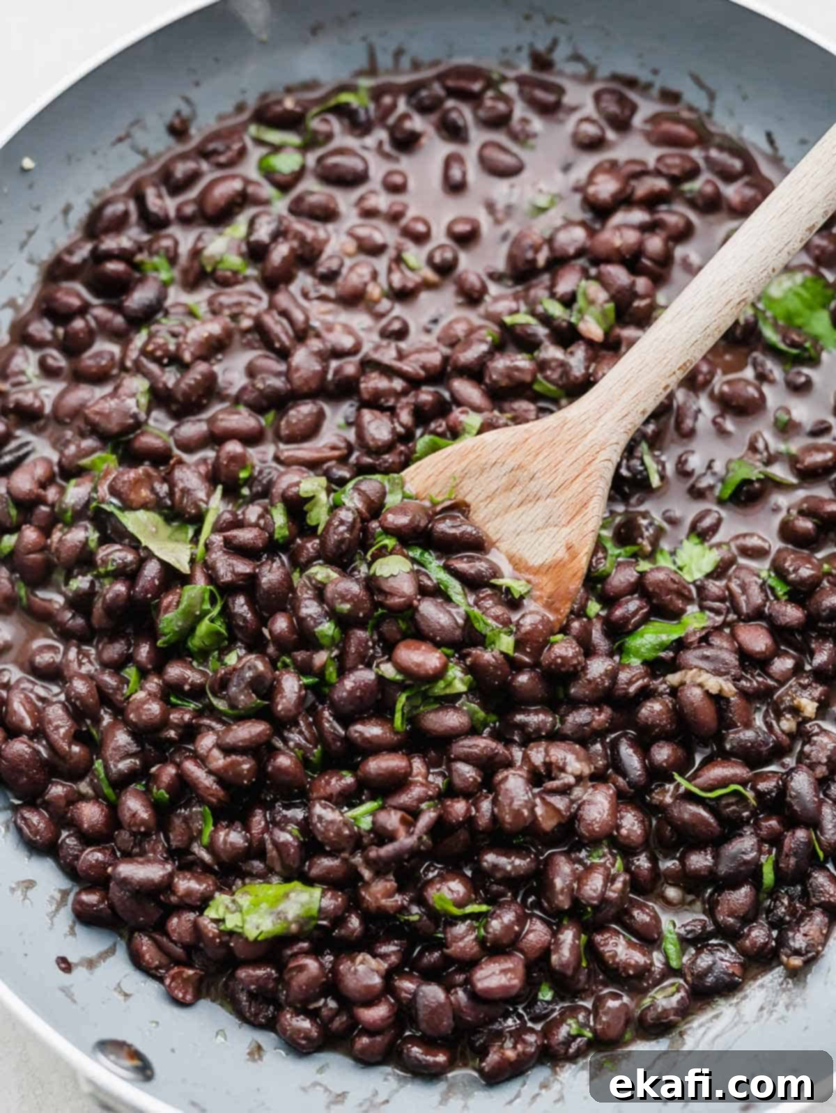 Cafe Rio Style Black Beans 6 A wooden spoon stirring cilantro-studded Cafe Rio Black Beans in a skillet.