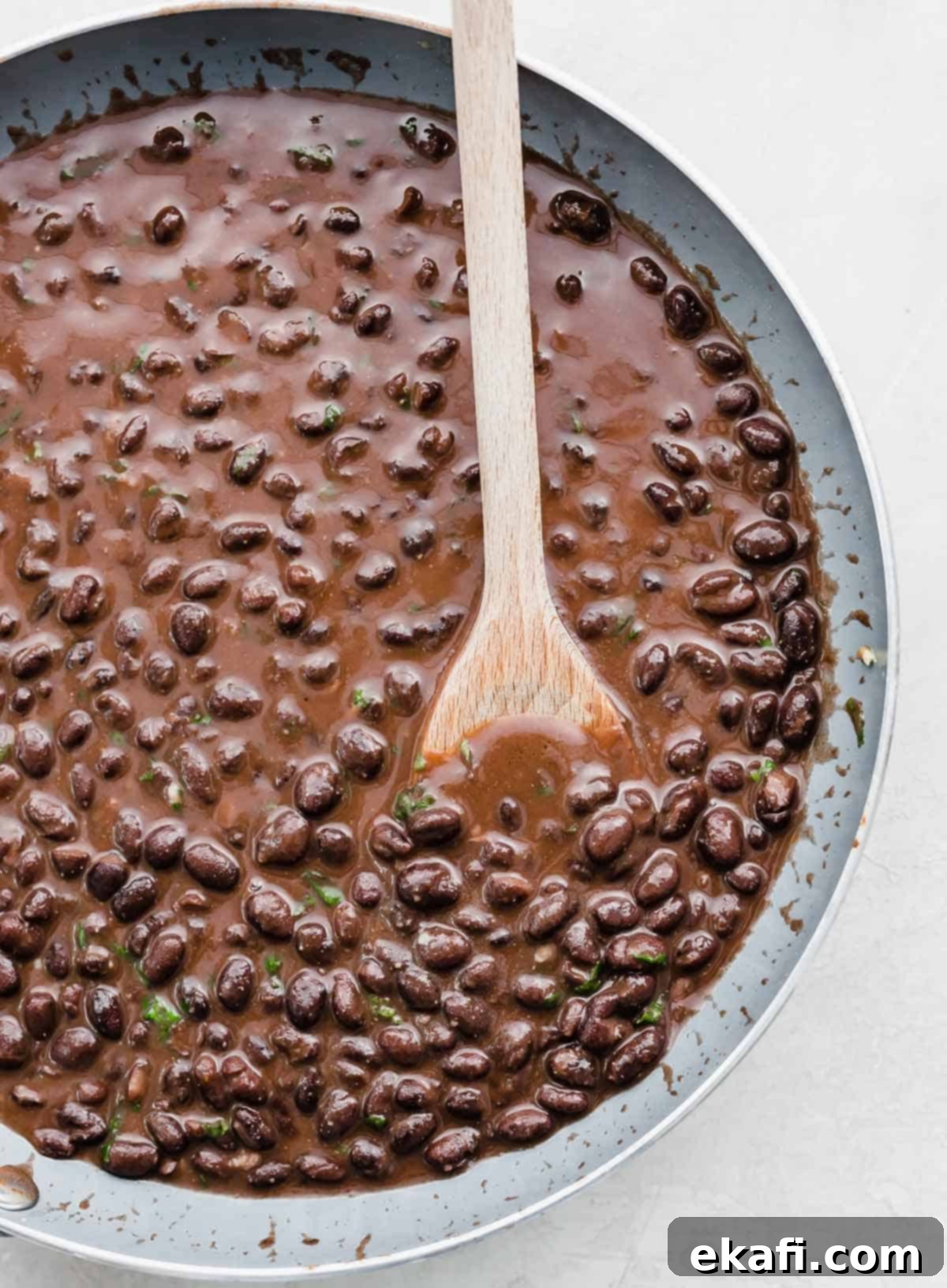 Cafe Rio Style Black Beans 7 A wooden spoon rests in a skillet brimming with delicious Cafe Rio Black Beans.
