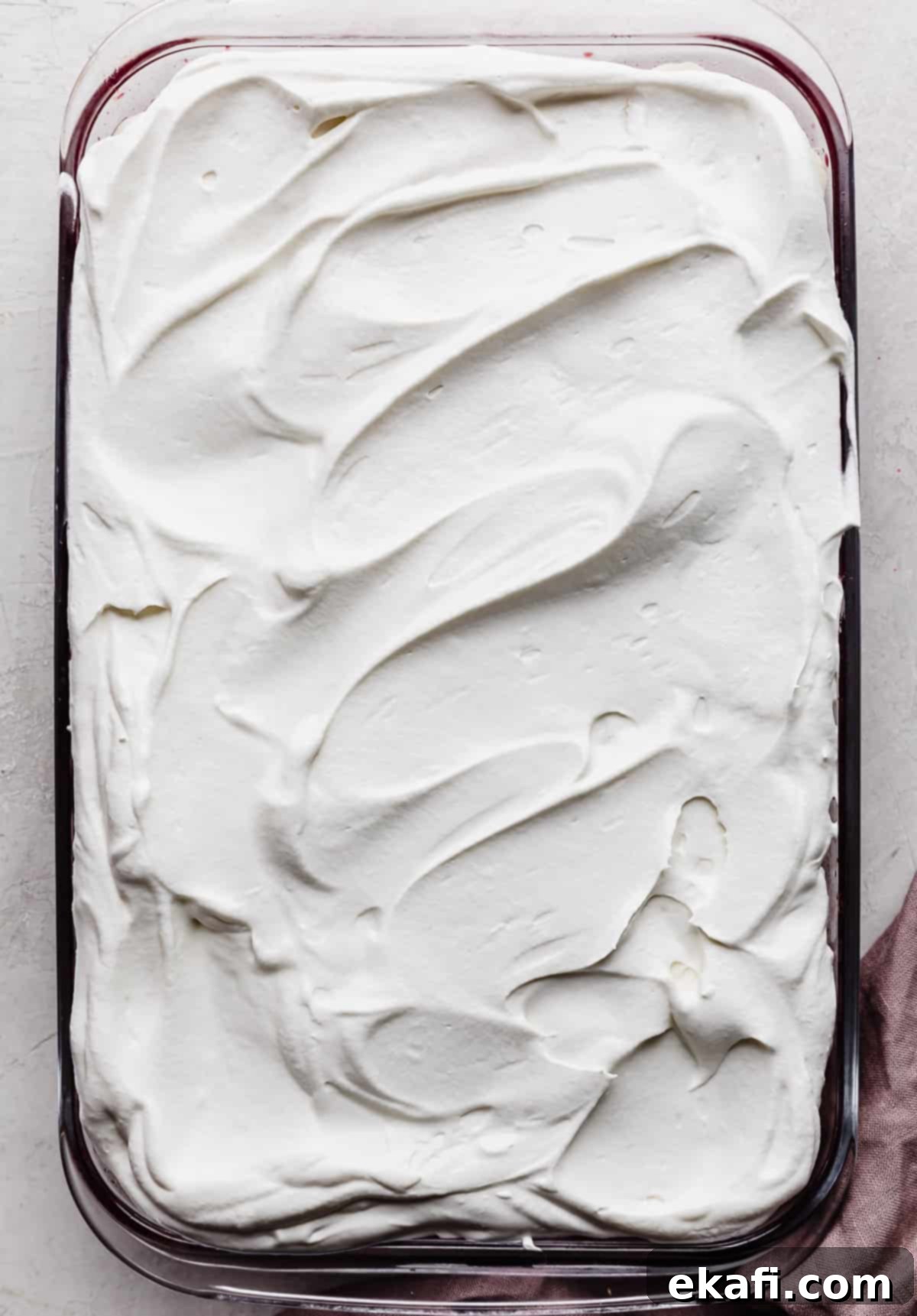Ruby Pomegranate Delight 11 Whipped cream covering a Pomegranate Jell-O in a glass rectangular baking dish.