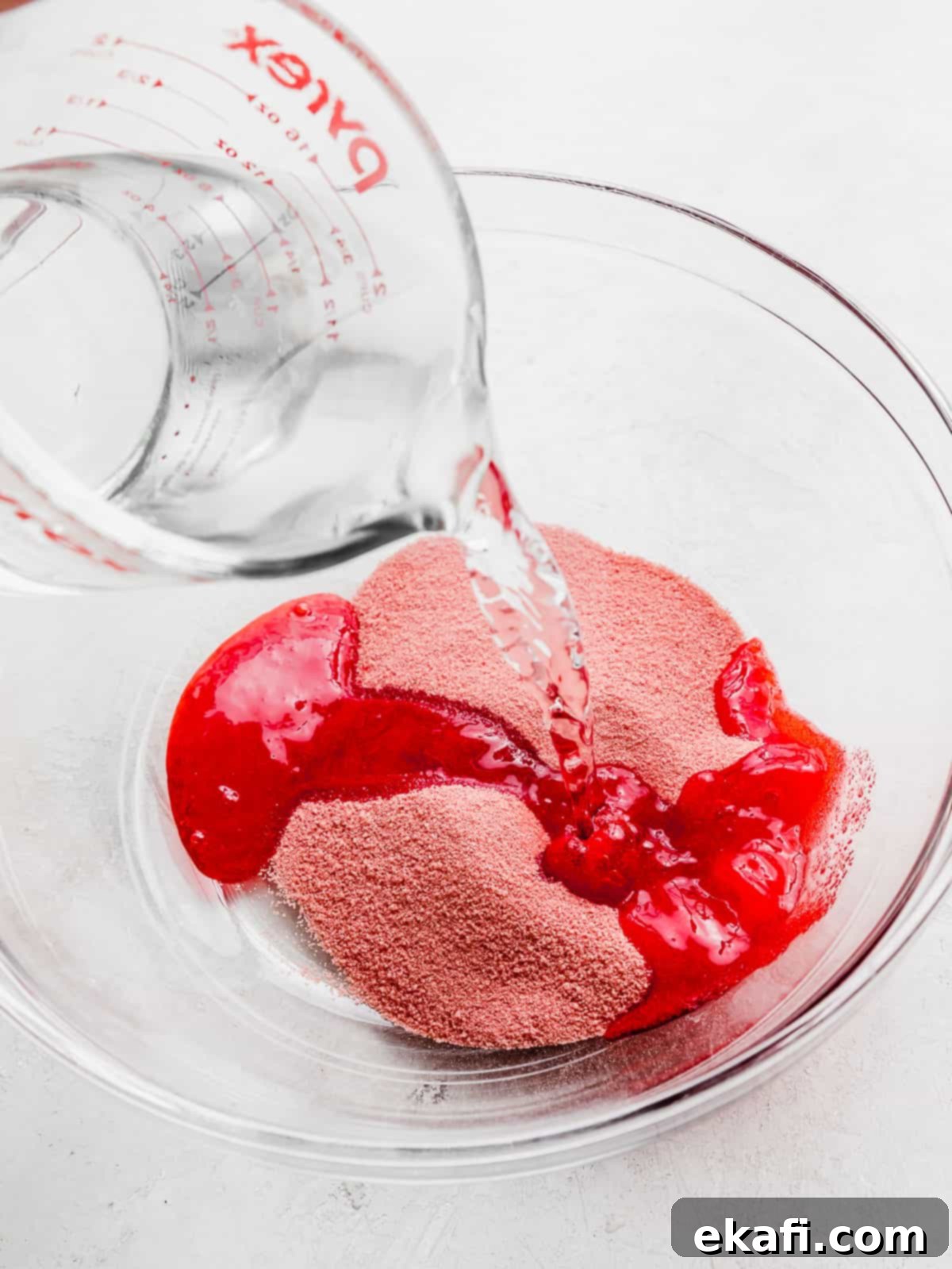Ruby Pomegranate Delight 4 Water pouring into a glass bowl with red Jell-O powder in it.