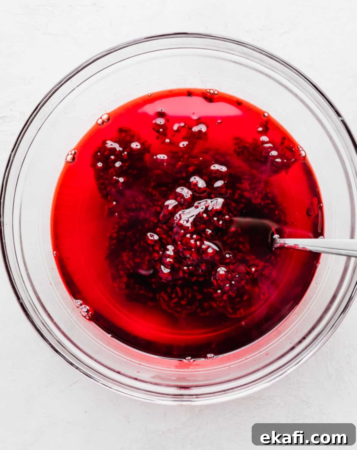 Ruby Pomegranate Delight 5 Bright red liquid jell-o with a raspberry topping sauce being stirred into it.