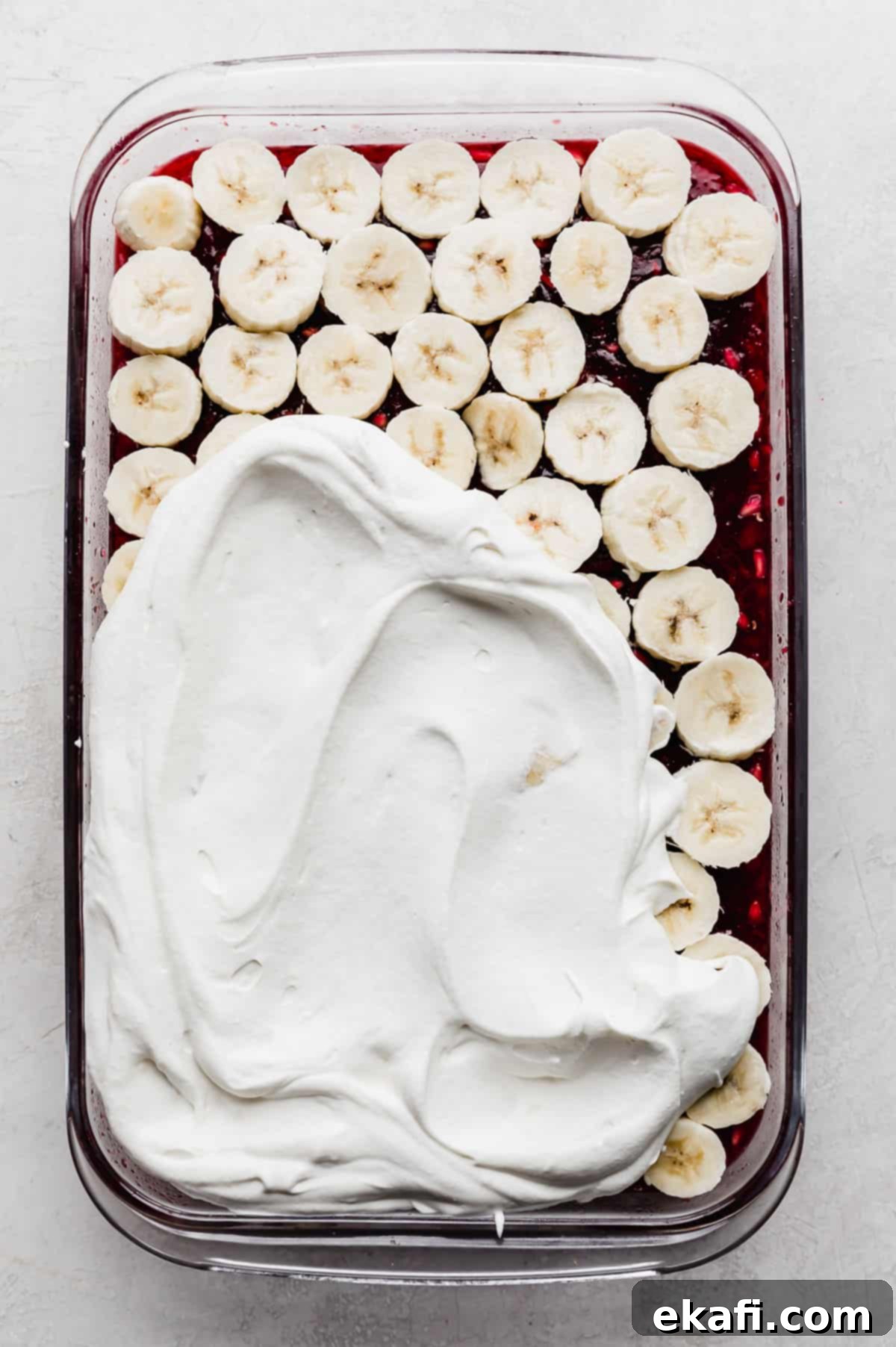 Ruby Pomegranate Delight 10 Whipped cream spread overtop half of the sliced bananas that are overtop the red Pomegranate Jell-O.
