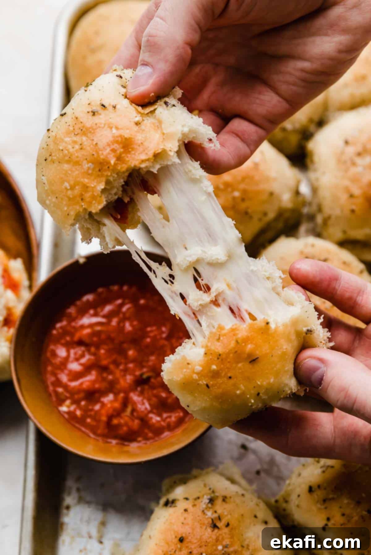 From-Scratch Pizza Rolls 2 Two hands pulling a homemade pizza roll apart, revealing the melty, stretchy mozzarella cheese and pepperoni inside.