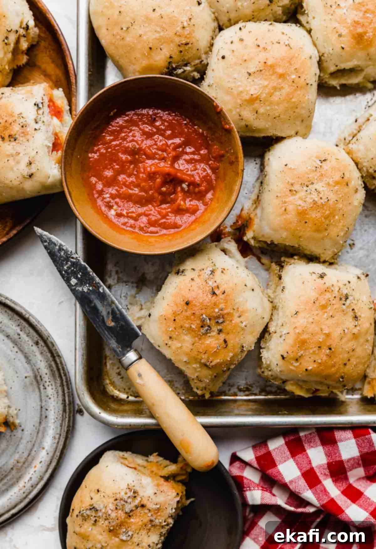From-Scratch Pizza Rolls 6 Overhead photo of a baking sheet topped with golden-brown pizza rolls, beside a small bowl of red dipping sauce.