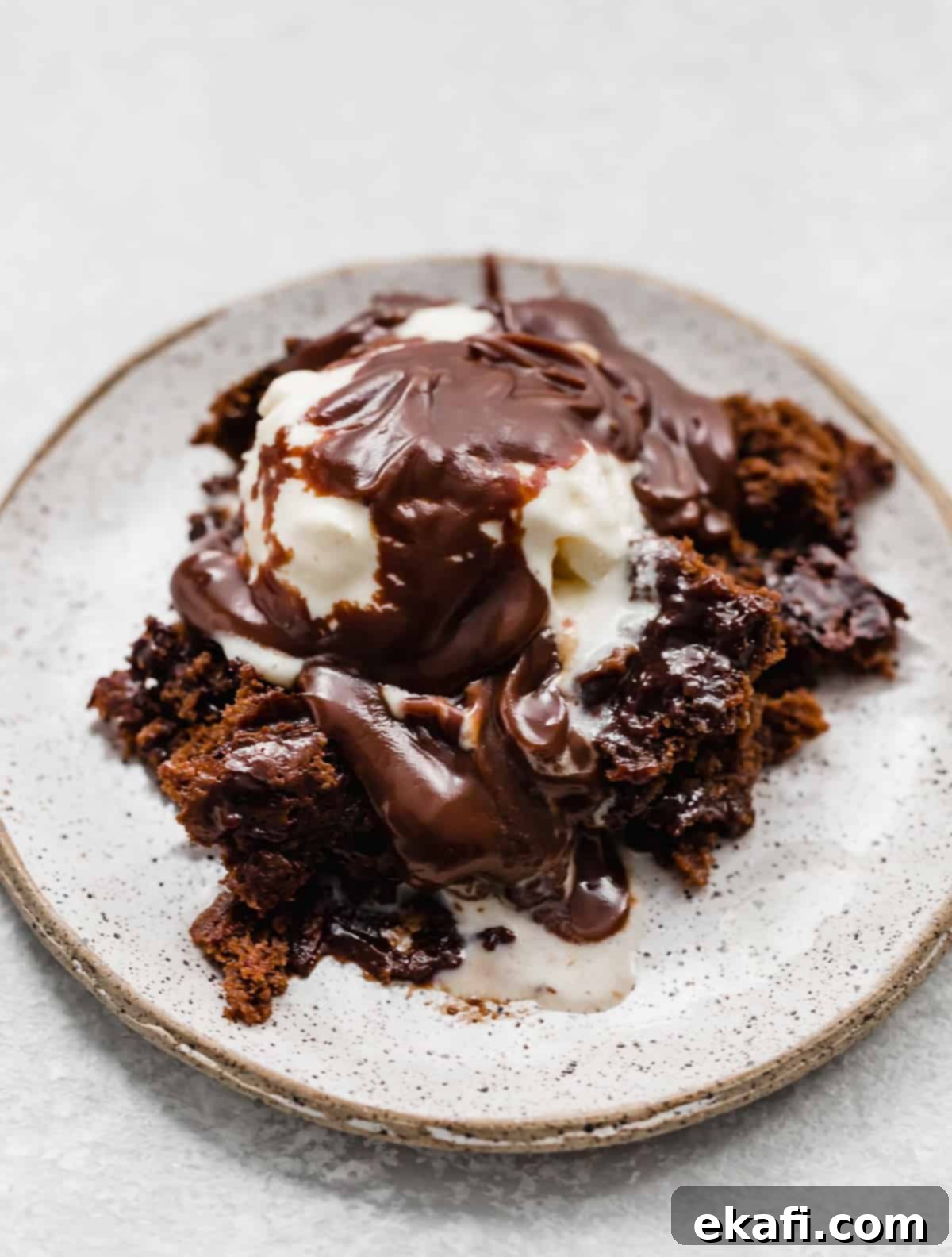 Κέικ με καυτή σοκολάτα 9 Hot Fudge Cake σε λευκό πιάτο με μια μπάλα παγωτό και ζεστή σάλτσα fudge περιχυμένη από πάνω.
