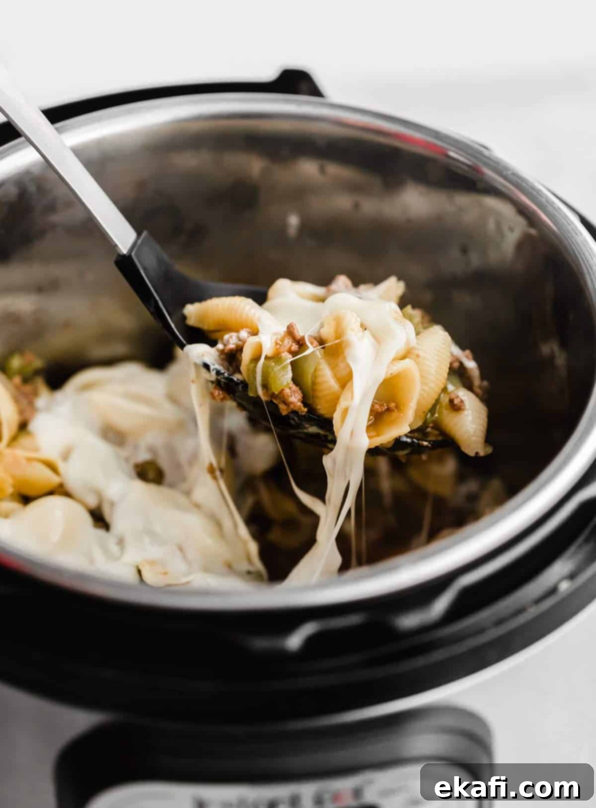 Creamy Instant Pot Philly Cheesesteak Pasta 2 A black serving spoon scooping up Instant Pot Philly Cheesesteak Pasta from an instant pot, showcasing the cheesy, beefy pasta.