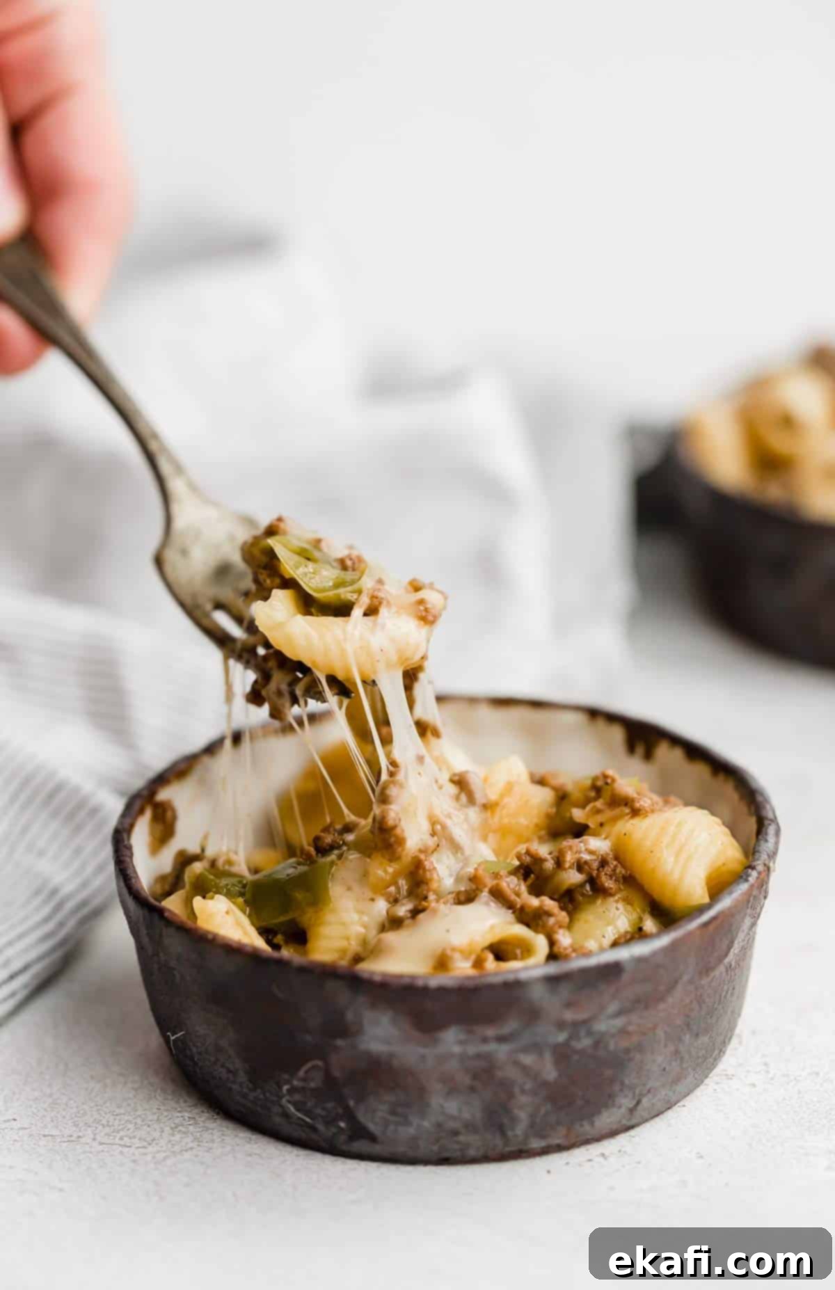 Creamy Instant Pot Philly Cheesesteak Pasta 5 A fork picking up a generous portion of Instant Pot Philly Cheesesteak Pasta from a black bowl on a white background, highlighting the melted cheese and beef.