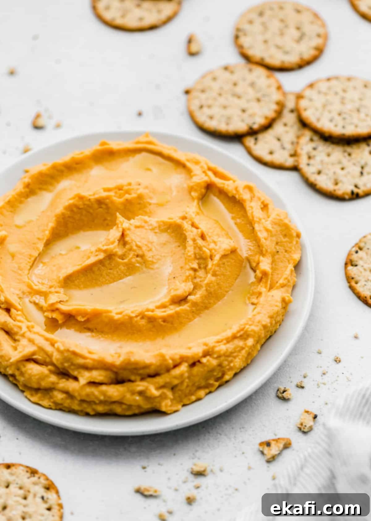 Sweet Potato Hummus 6 Sweet Potato Hummus elegantly presented on a plate, surrounded by an assortment of crunchy crackers, ready for dipping.