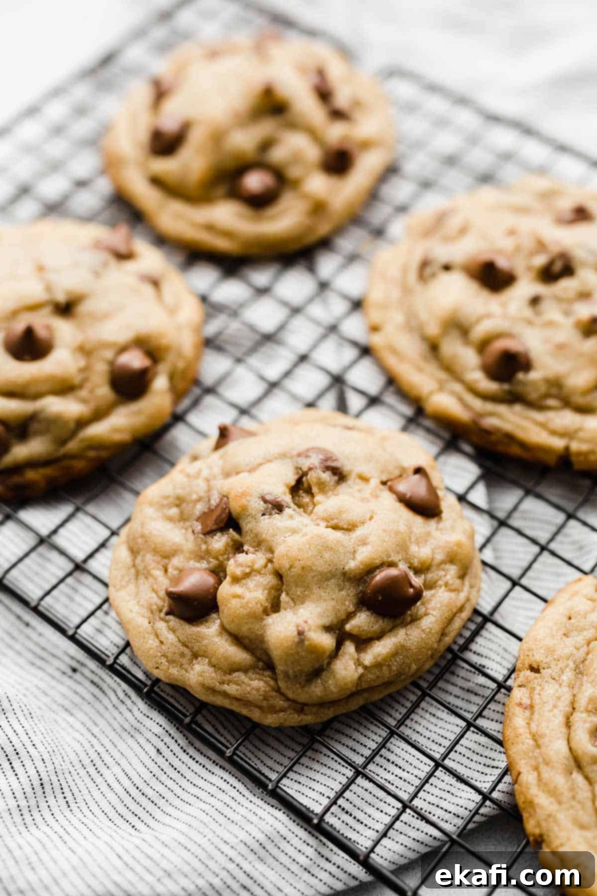 Copycat Crumbl Chocolate Chip Cookie Perfection 12 Multiple freshly baked Crumbl Chocolate Chip Cookies cooling on a black wire rack, showcasing their uniform size and golden-brown finish.