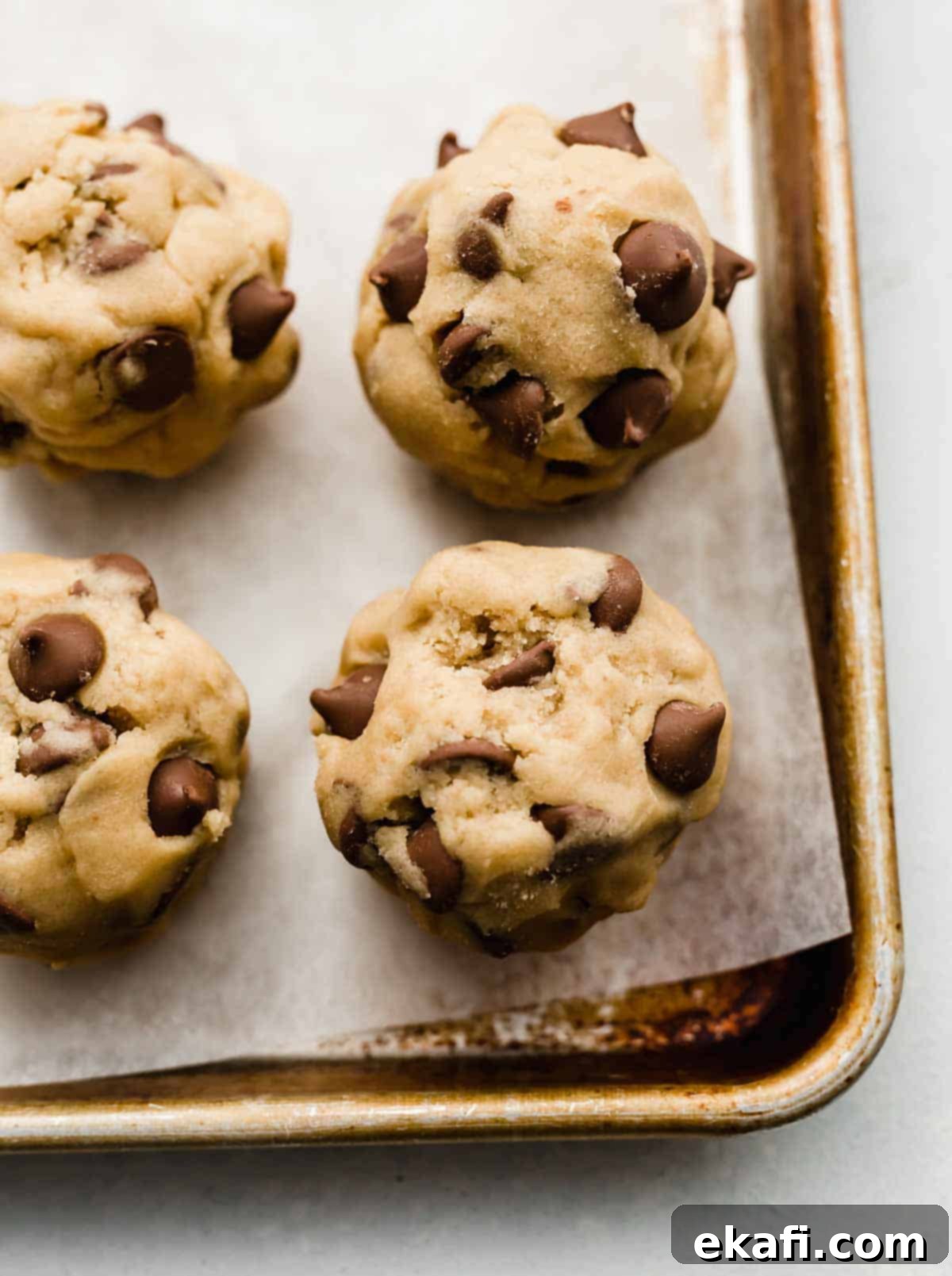 Copycat Crumbl Chocolate Chip Cookie Perfection 8 Large Crumbl Chocolate Chip Cookie dough balls arranged neatly on a parchment lined baking sheet, ready for baking.