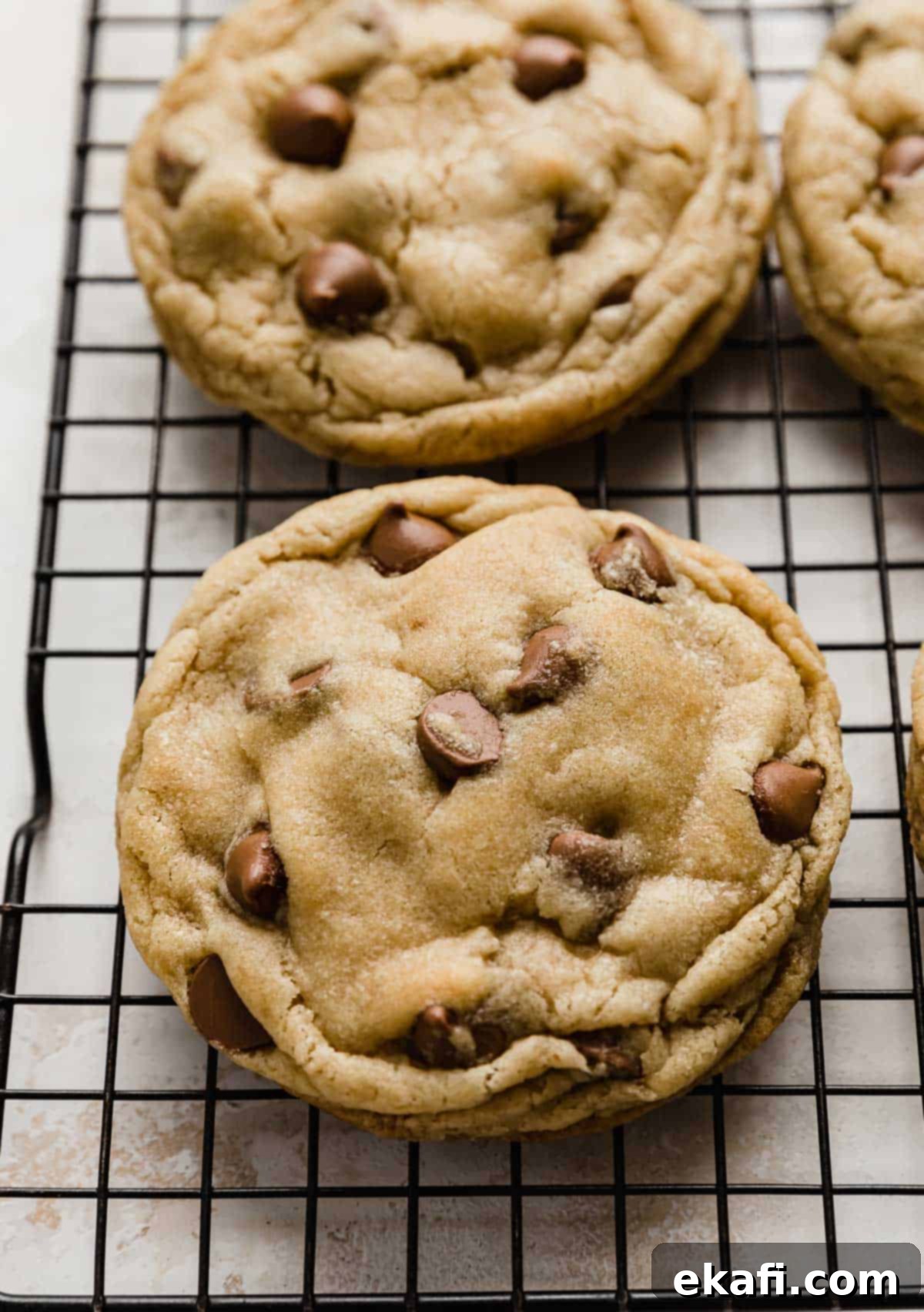 Copycat Crumbl Chocolate Chip Cookie Perfection 9 A freshly baked, large copycat Crumbl Chocolate Chip Cookie cooling on a black wire rack.