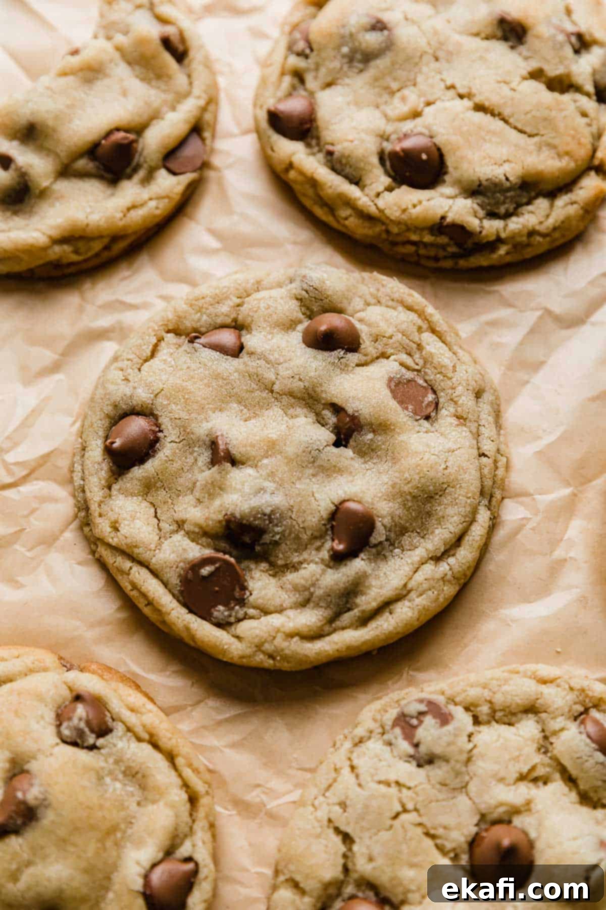 Copycat Crumbl Chocolate Chip Cookie Perfection 10 A freshly baked Crumbl Chocolate Chip Cookie resting on a tan parchment paper, showcasing its perfect golden-brown edges and melted chocolate.