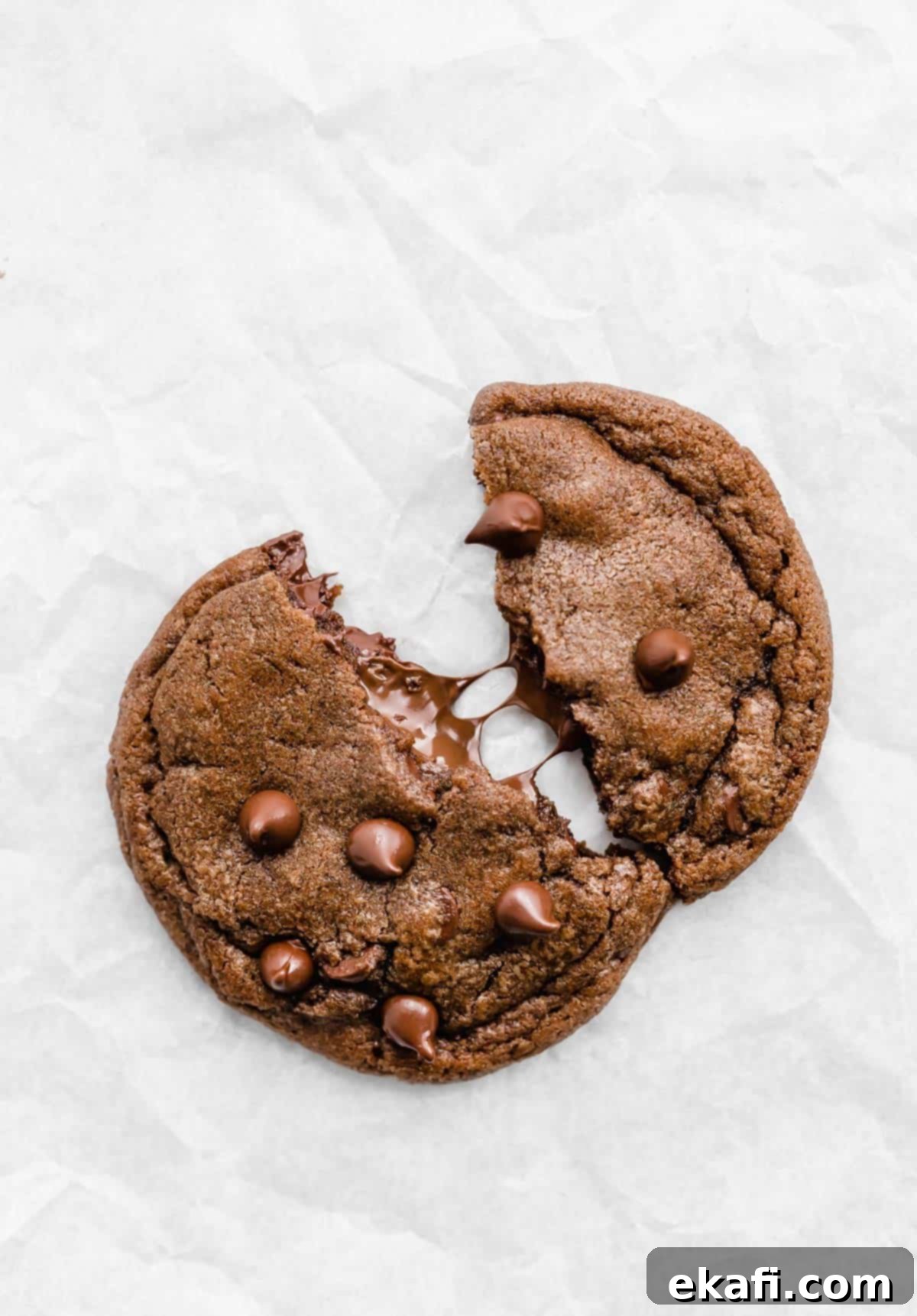 Nutella Lava Kurabiyeleri 2 A perfectly baked Nutella Stuffed Nutella Cookie, split in half to reveal the warm, molten Nutella center, resting on white parchment paper.