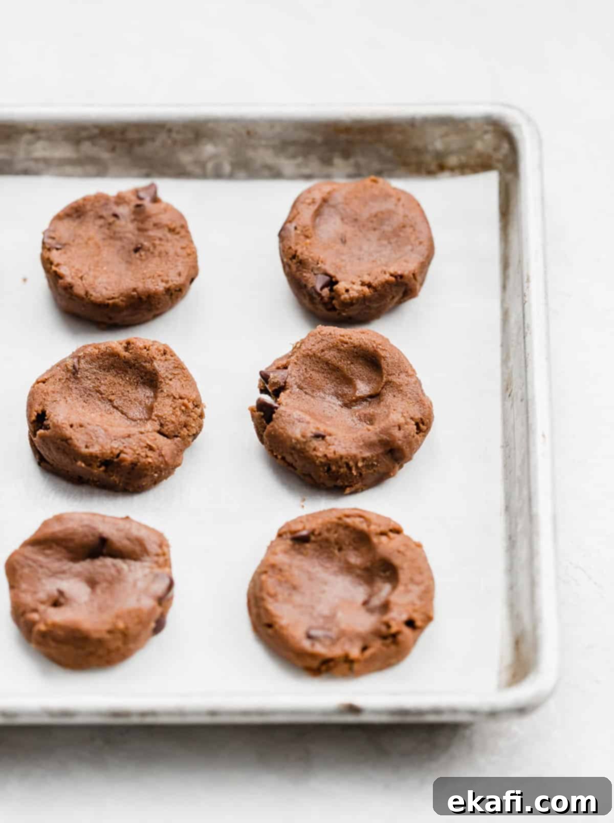 Nutella Lava Kurabiyeleri 4 Flattened Nutella cookie dough disks, some with indentations for filling, arranged on a baking sheet lined with parchment paper.