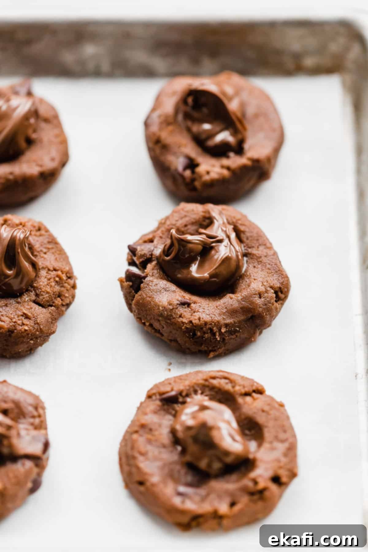 Nutella Lava Kurabiyeleri 5 A close-up of raw Nutella cookie dough disks with a teaspoon of Nutella perfectly placed in the center of each, ready to be covered.