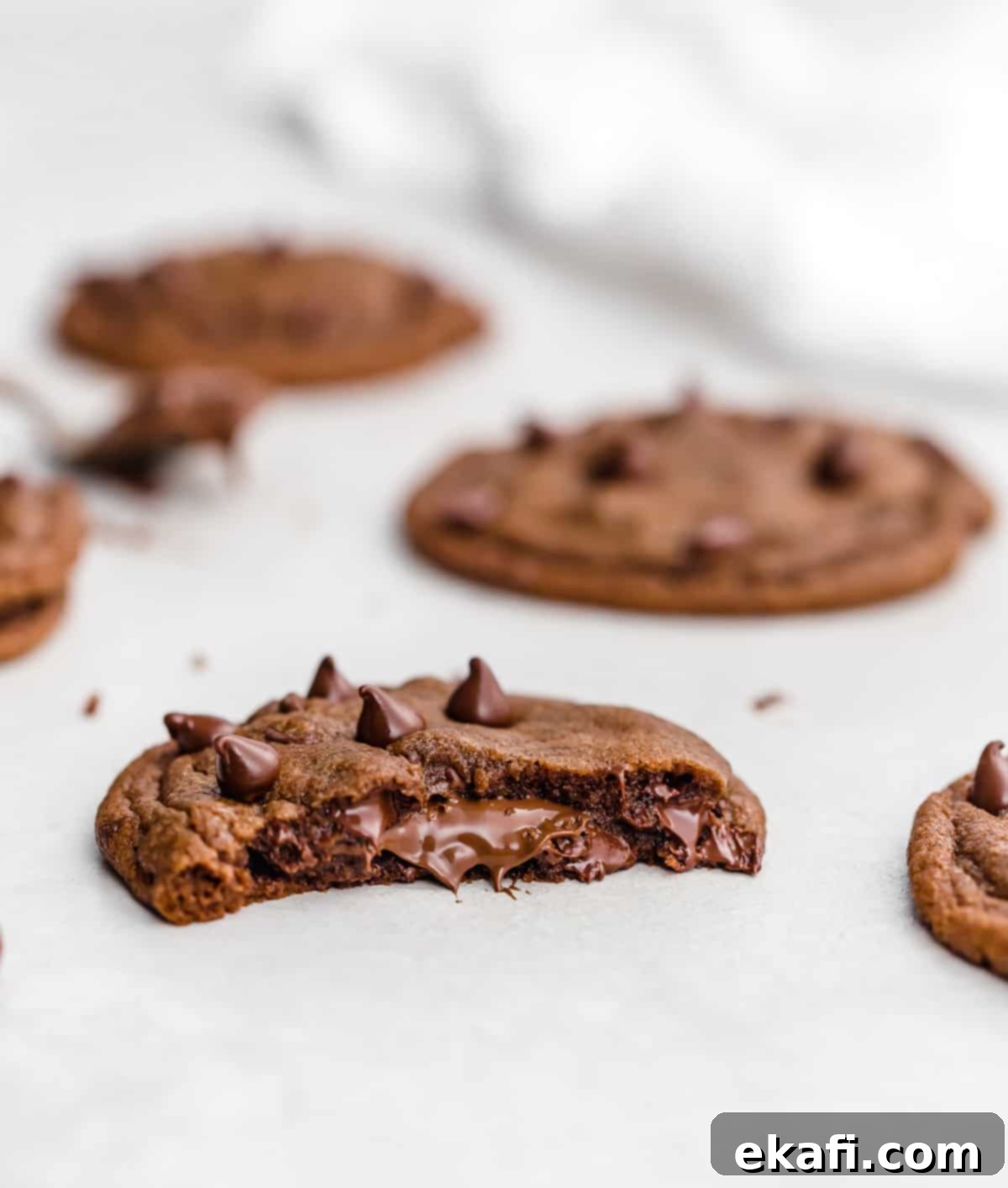 Nutella Lava Kurabiyeleri 8 A Nutella Stuffed Nutella Cookie, perfectly halved to showcase its incredibly rich and gooey Nutella filling, resting on a clean white surface.