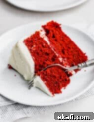 Heirloom Red Velvet Cake 11 A slice of the best layered red velvet cake topped with white frosting on a white plate, showcasing its fluffy texture and vibrant color.