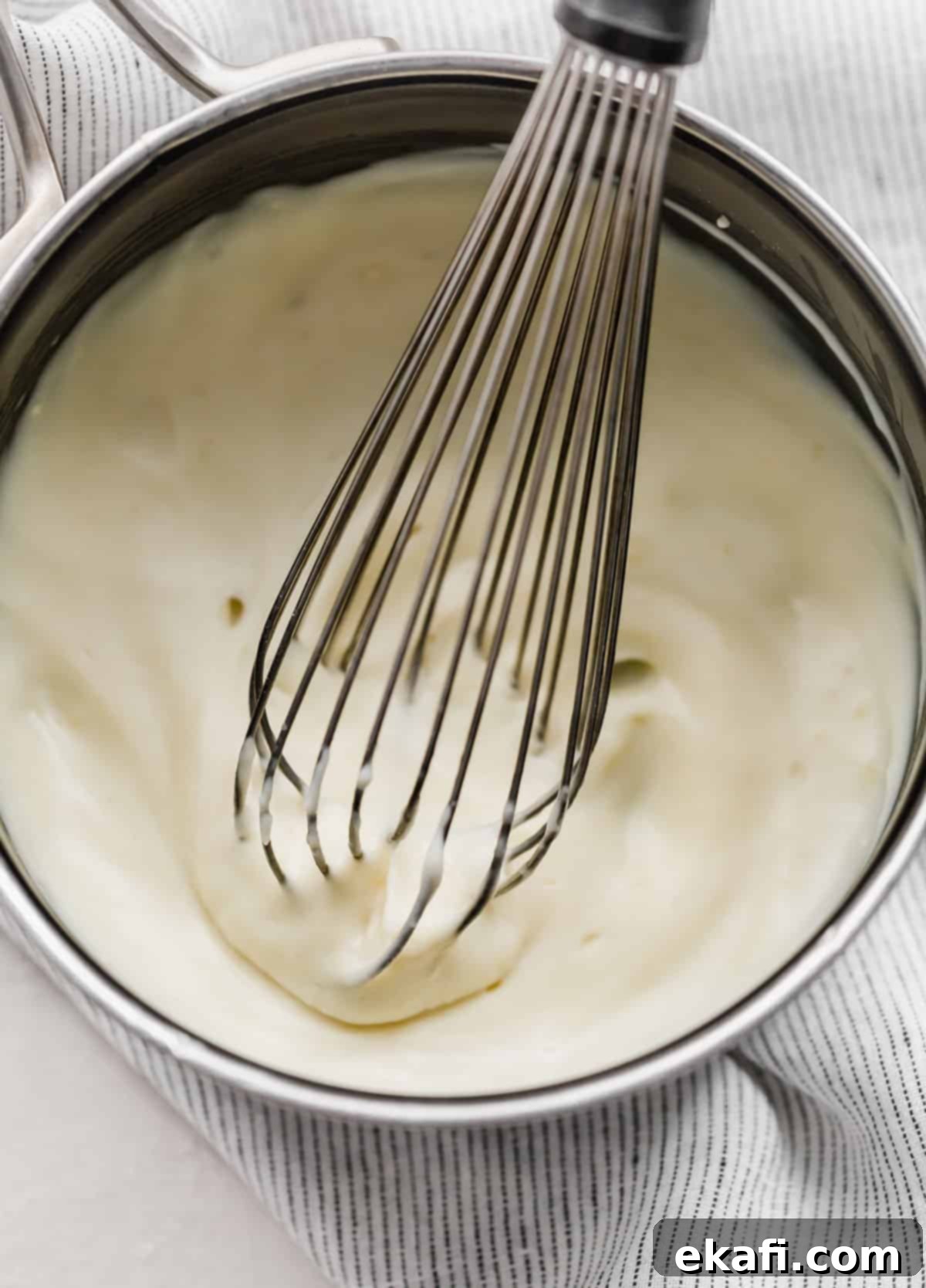 Heirloom Red Velvet Cake 7 A whisk stirring a thick, white flour and milk mixture in a saucepan, demonstrating the making of the old fashioned frosting base.