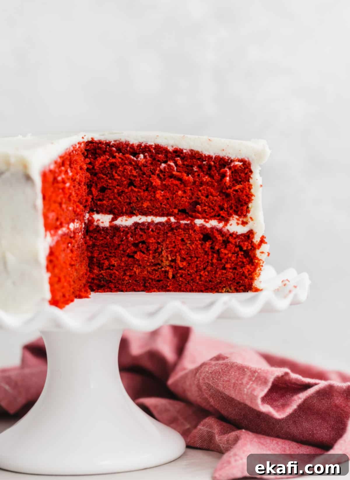 Heirloom Red Velvet Cake 9 A two-tiered Old Fashioned Red Velvet Cake, elegantly frosted with classic white icing and presented on a white cake stand, inviting a slice.