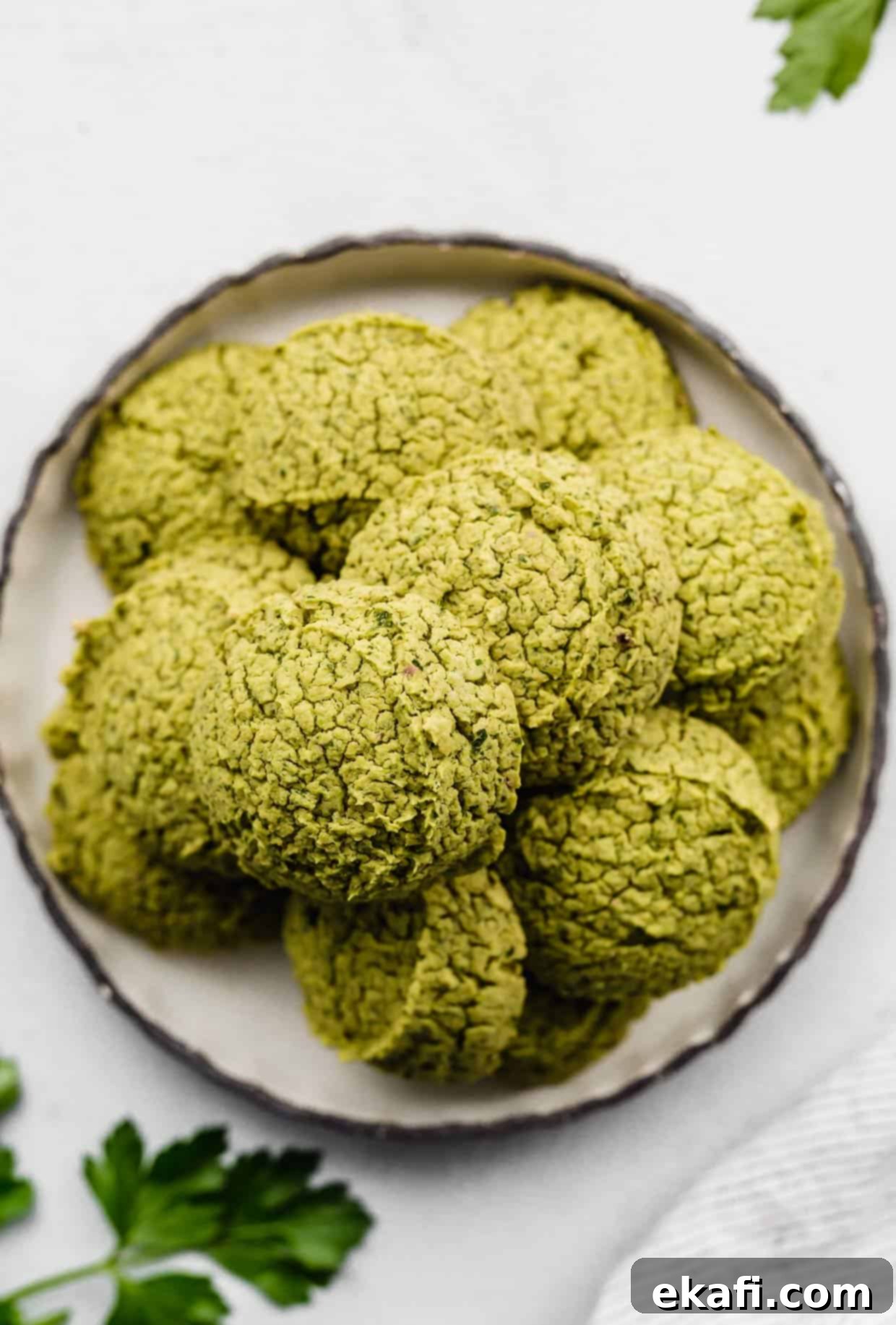 Fresh Herb Falafel 2 Green Baked Falafel rounds on a black rimmed white plate on a white background.