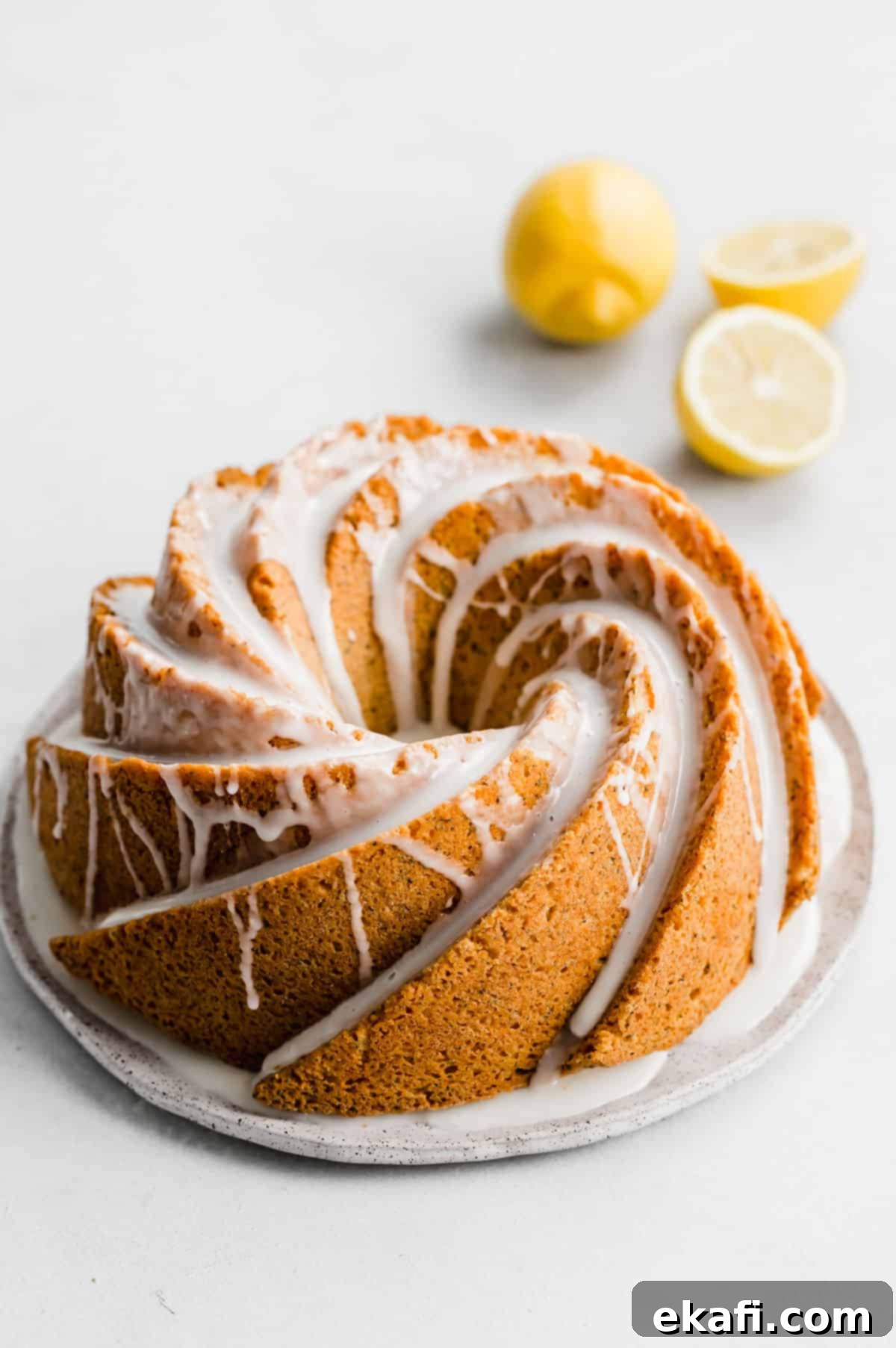 Zesty Lemon Poppy Seed Crown 6 A Lemon Poppy Seed Bundt Cake topped with a white glaze on a white plate on a white background.