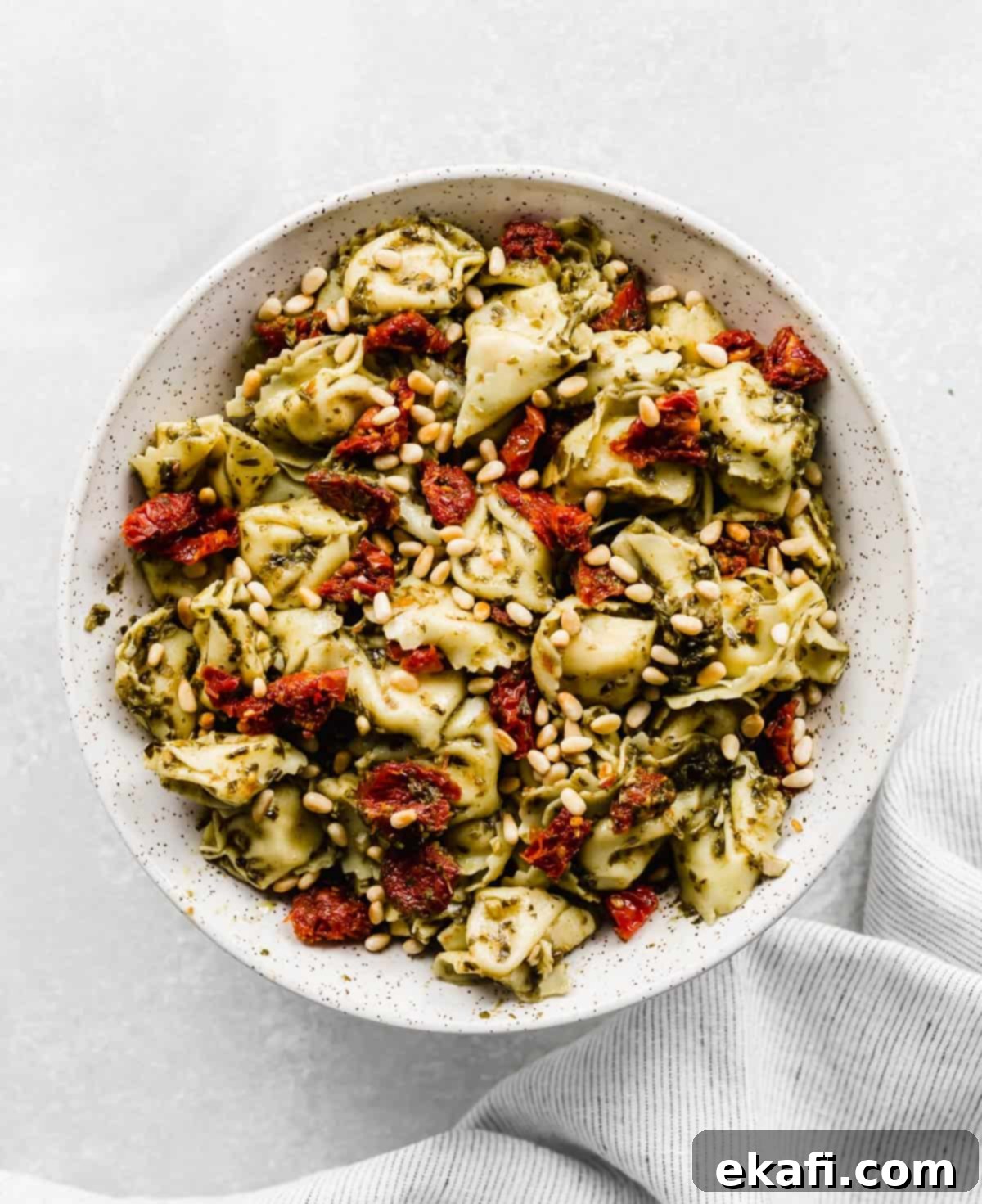 Pesto-Kissed Tortellini 4 A large bowl with Pesto Tortellini Pasta Salad with pine nuts and sun-dried tomatoes.