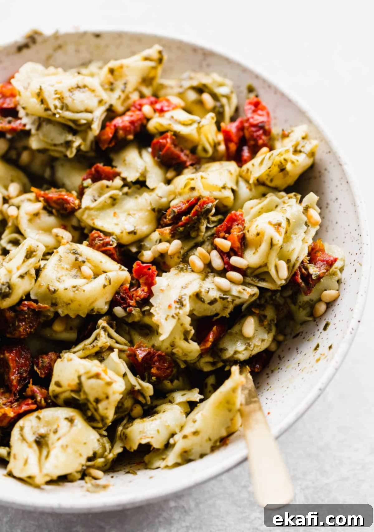 Pesto-Kissed Tortellini 5 A close up photo of Pesto Tortellini Pasta Salad with sun-dried tomatoes and pine nuts in the salad.
