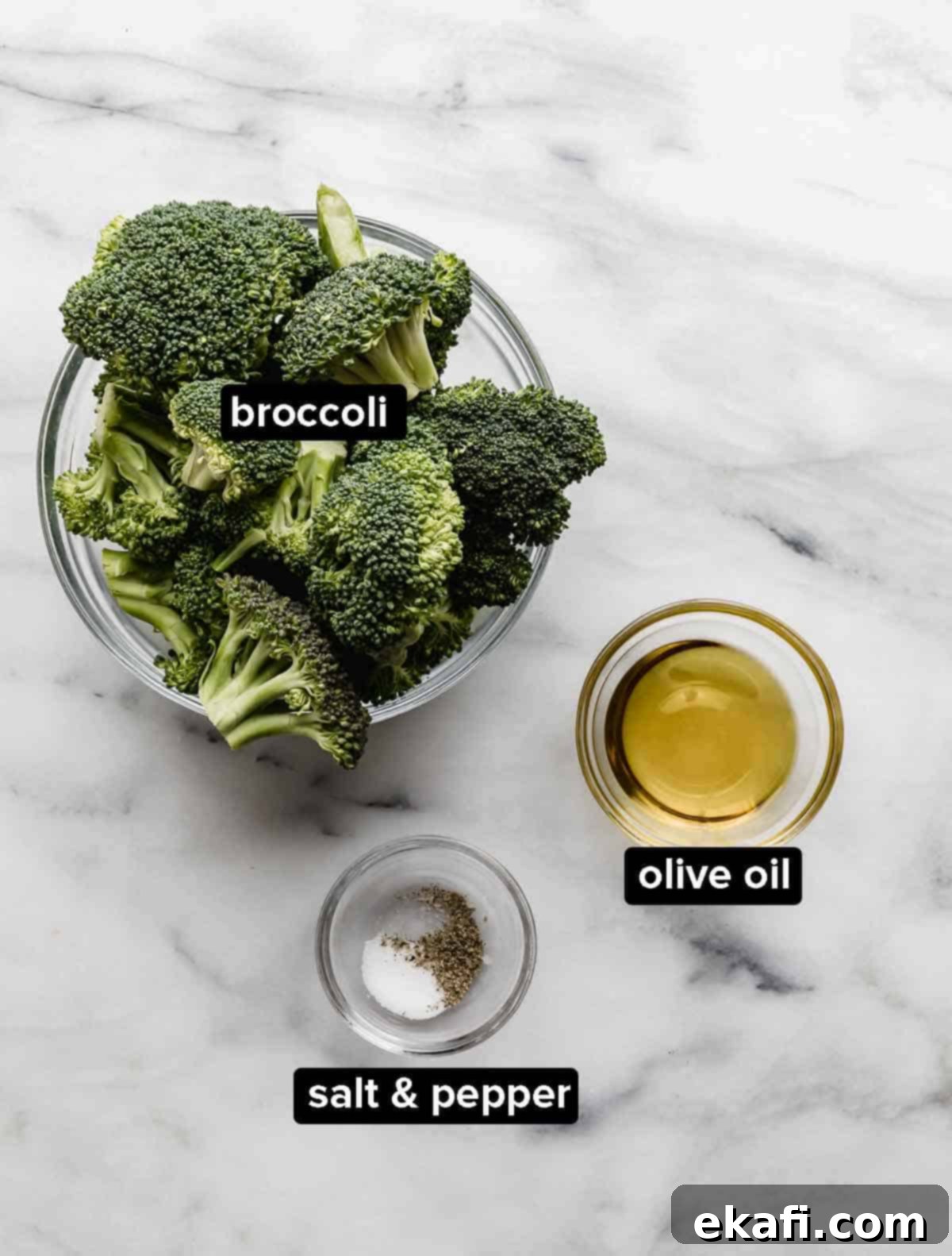 Crispy Oven Roasted Broccoli 3 Oven Roasted Broccoli ingredients on a white marble background: fresh broccoli florets, quality olive oil, kosher salt, and freshly ground black pepper.