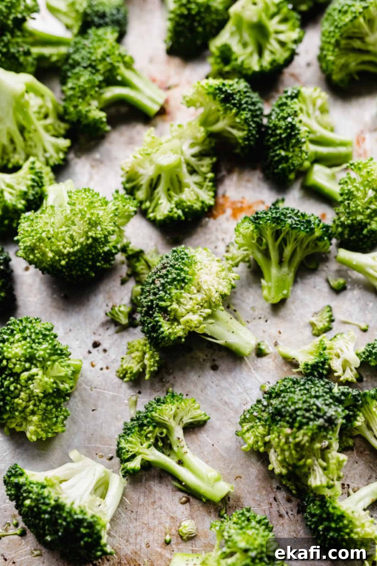 Crispy Oven Roasted Broccoli 4 Raw and uncooked broccoli florets spread in a single layer on a baking sheet, ready for roasting.