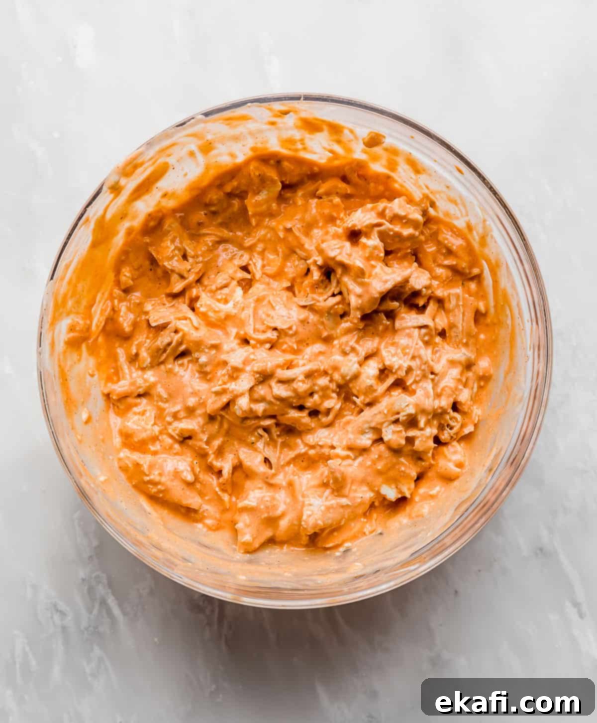 Ultimate Buffalo Chicken Dip 5 Bright orange Buffalo Chicken Dip mixture in a glass bowl on a white marble background.