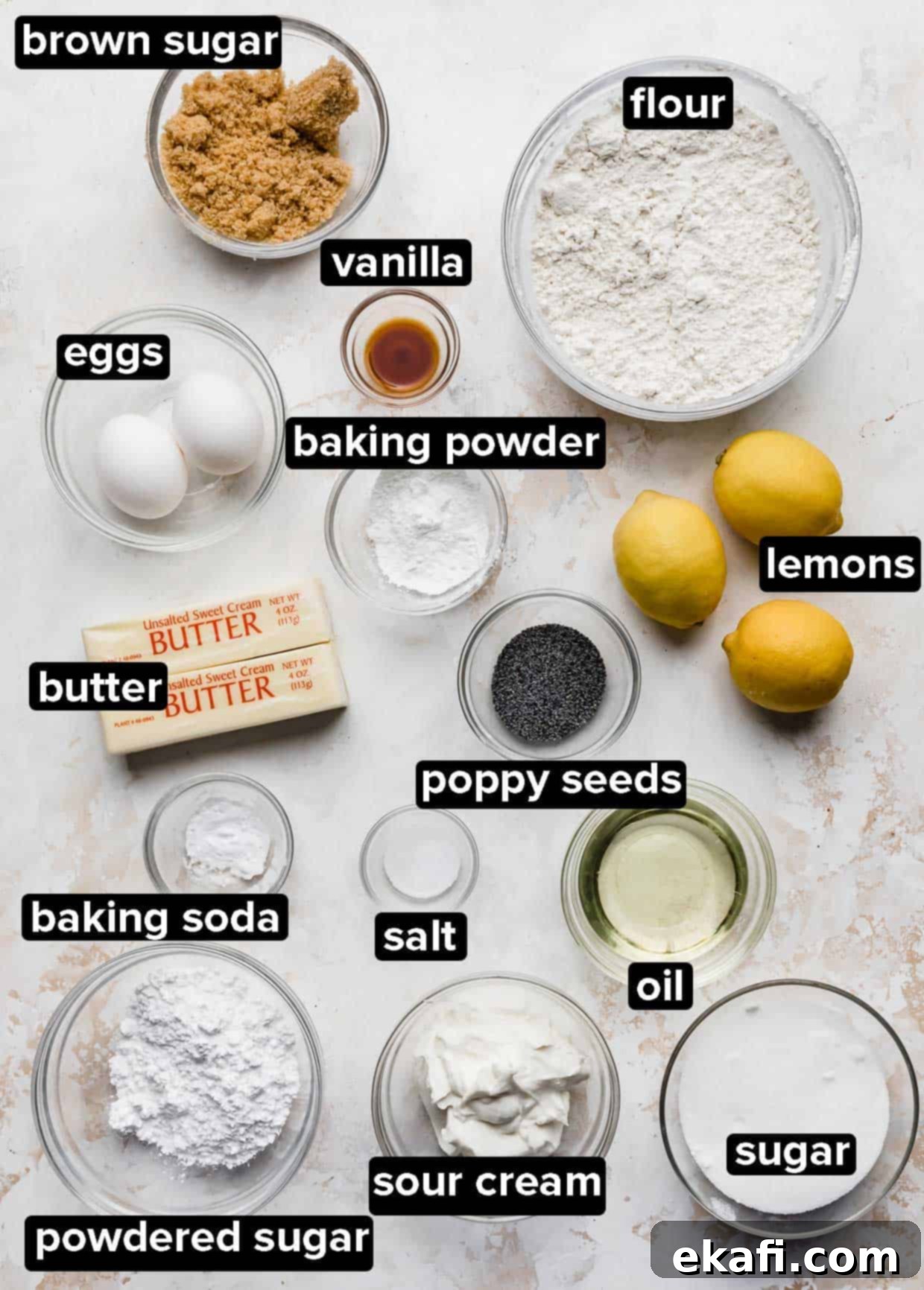 Ultra Moist Lemon Poppy Seed Muffins with Sour Cream 3 All the pre-measured ingredients for Lemon Poppy Seed Muffins, including butter, flour, sugar, lemons, and poppy seeds, neatly arranged in glass bowls on a white textured background.