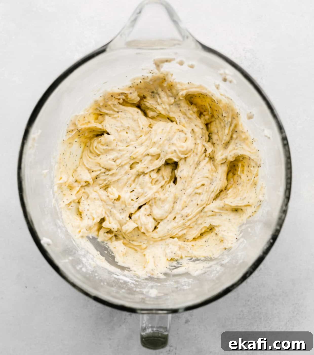 Ultra Moist Lemon Poppy Seed Muffins with Sour Cream 5 Creamy Lemon Poppy Seed Muffin batter in a glass mixing bowl, speckled with poppy seeds and lemon zest, on a white background.